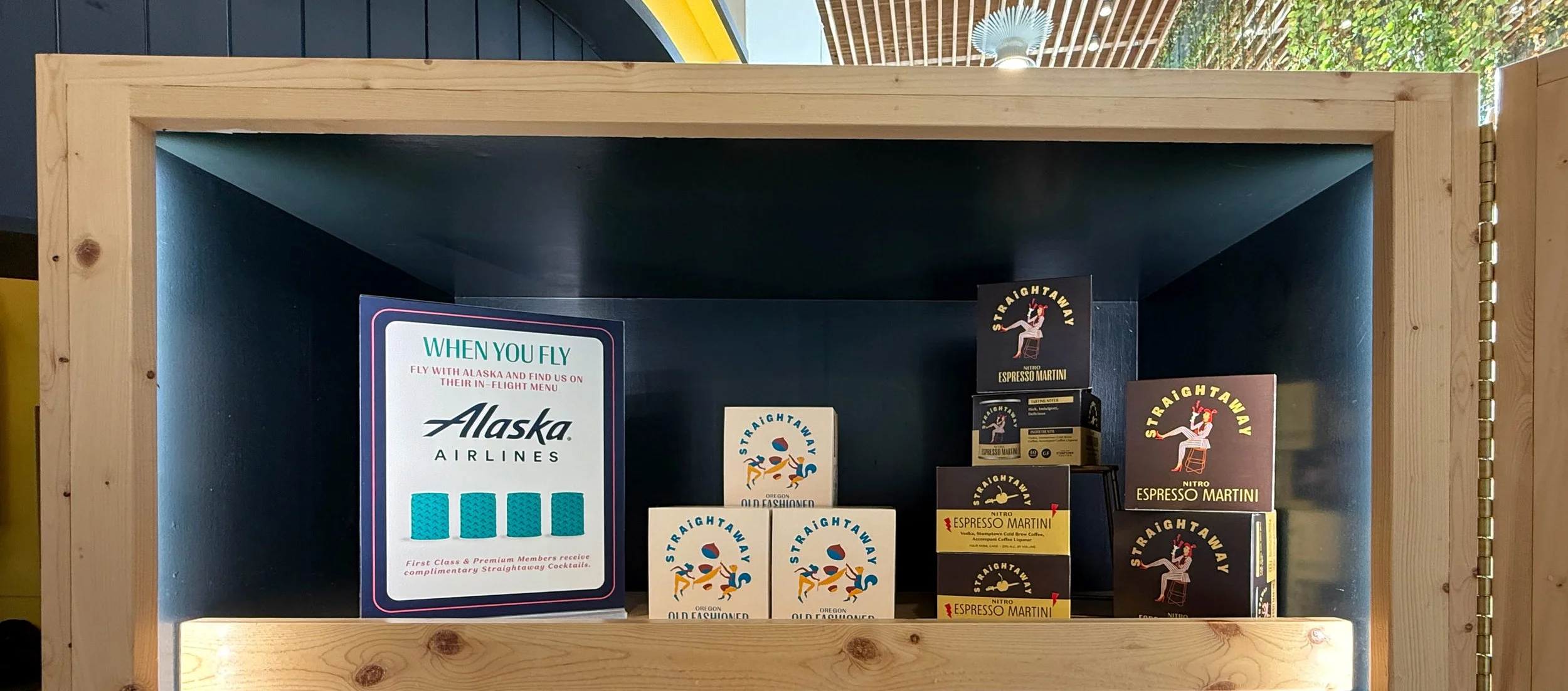Shelf displaying various boxes of Straightaway Nitro Espresso Martini mix with signage for Alaska Airlines promotion in the background.