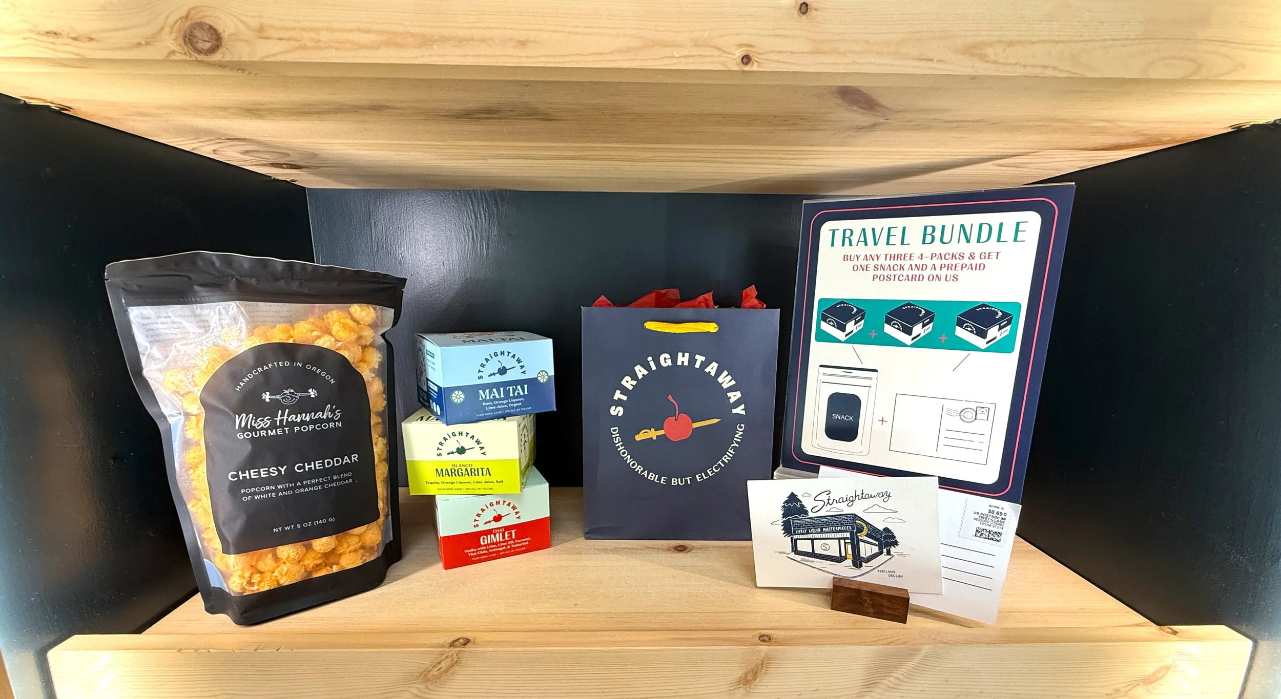A display shelf with gourmet popcorn, small boxes of condiments, a shopping bag, and a travel bundle flyer.