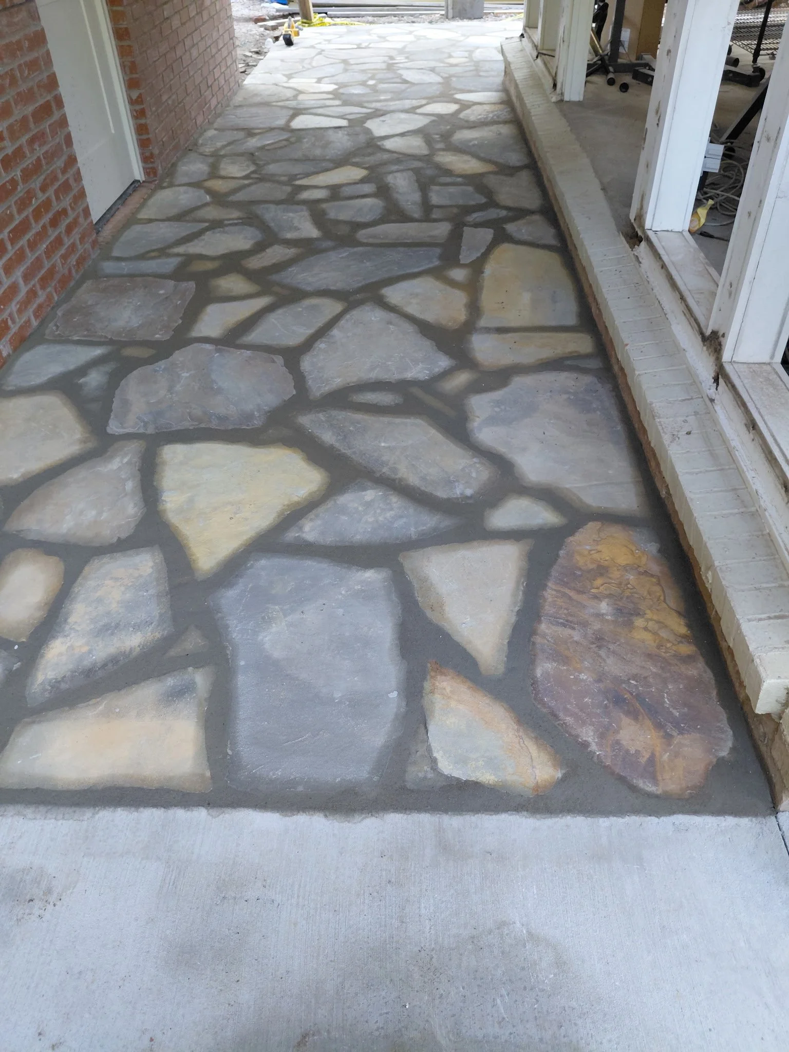 Newly installed flagstone patio extension on a concrete surface next to a brick house and sliding door.