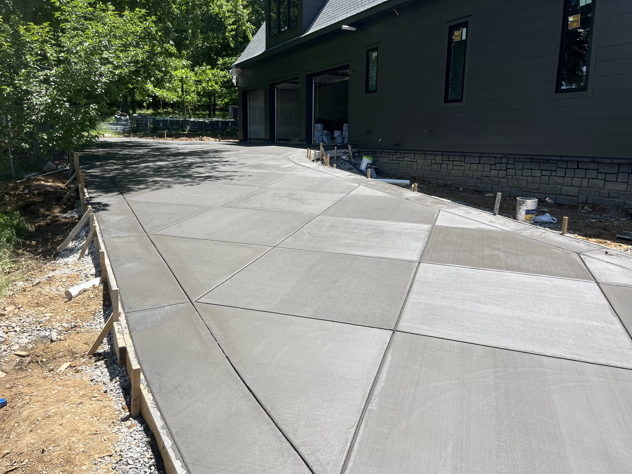 Newly poured concrete driveway with construction markers and a house in the background.