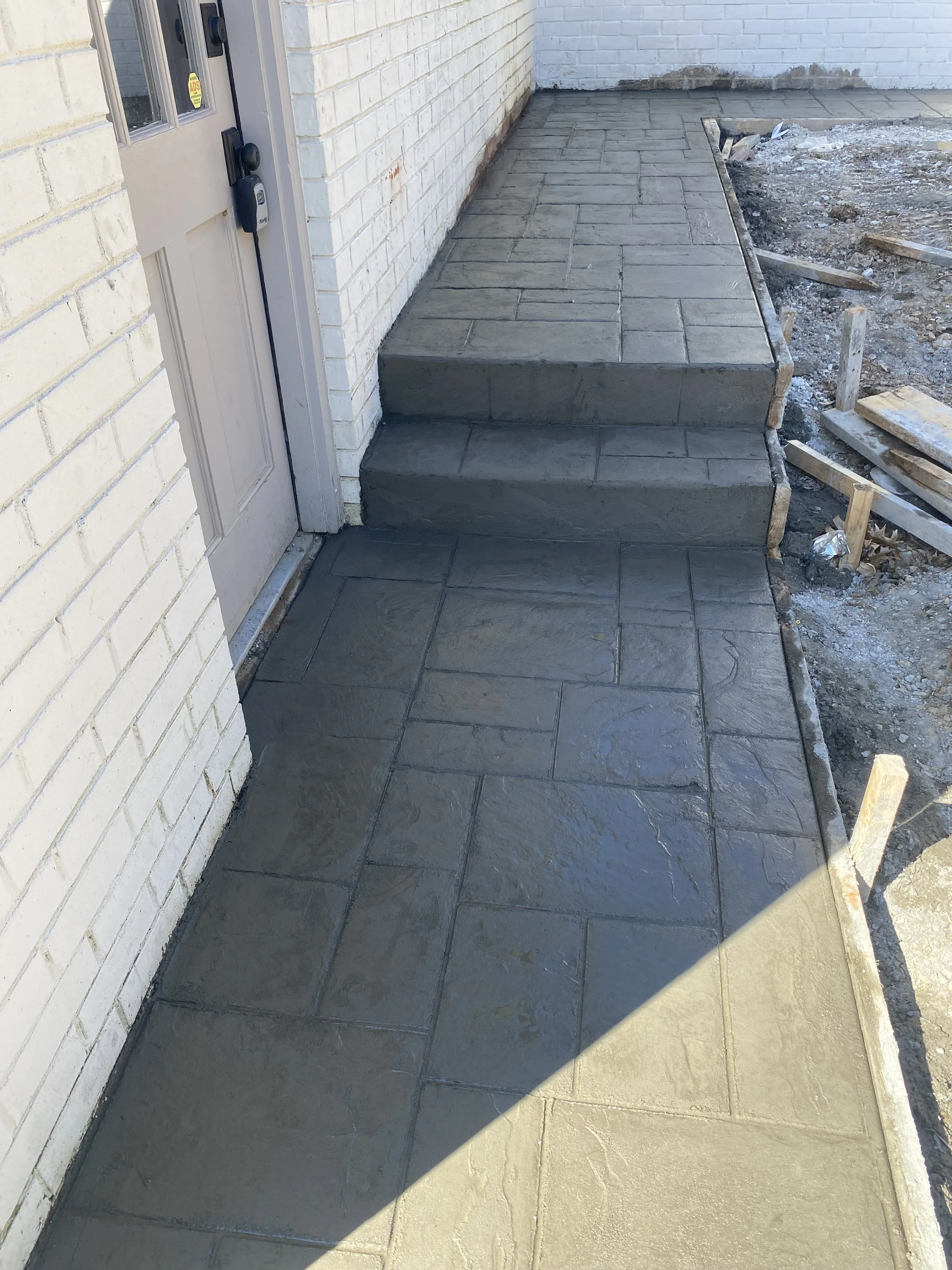 Newly installed concrete stairs and walkway leading to a door on a brick house.