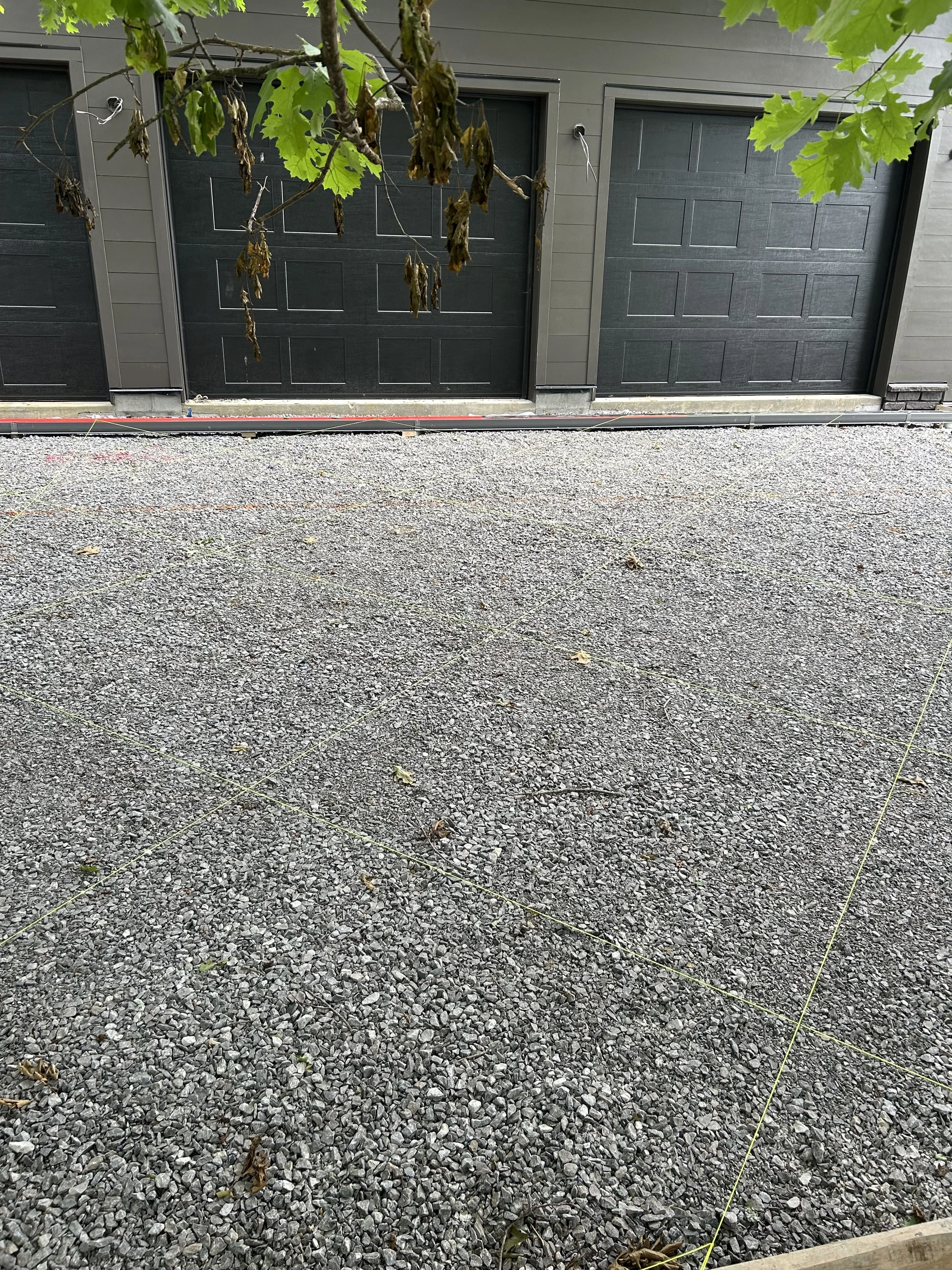 View of a gravel driveway in front of two dark-colored garage doors, with a tree branch and leaves partially visible at the top of the image.