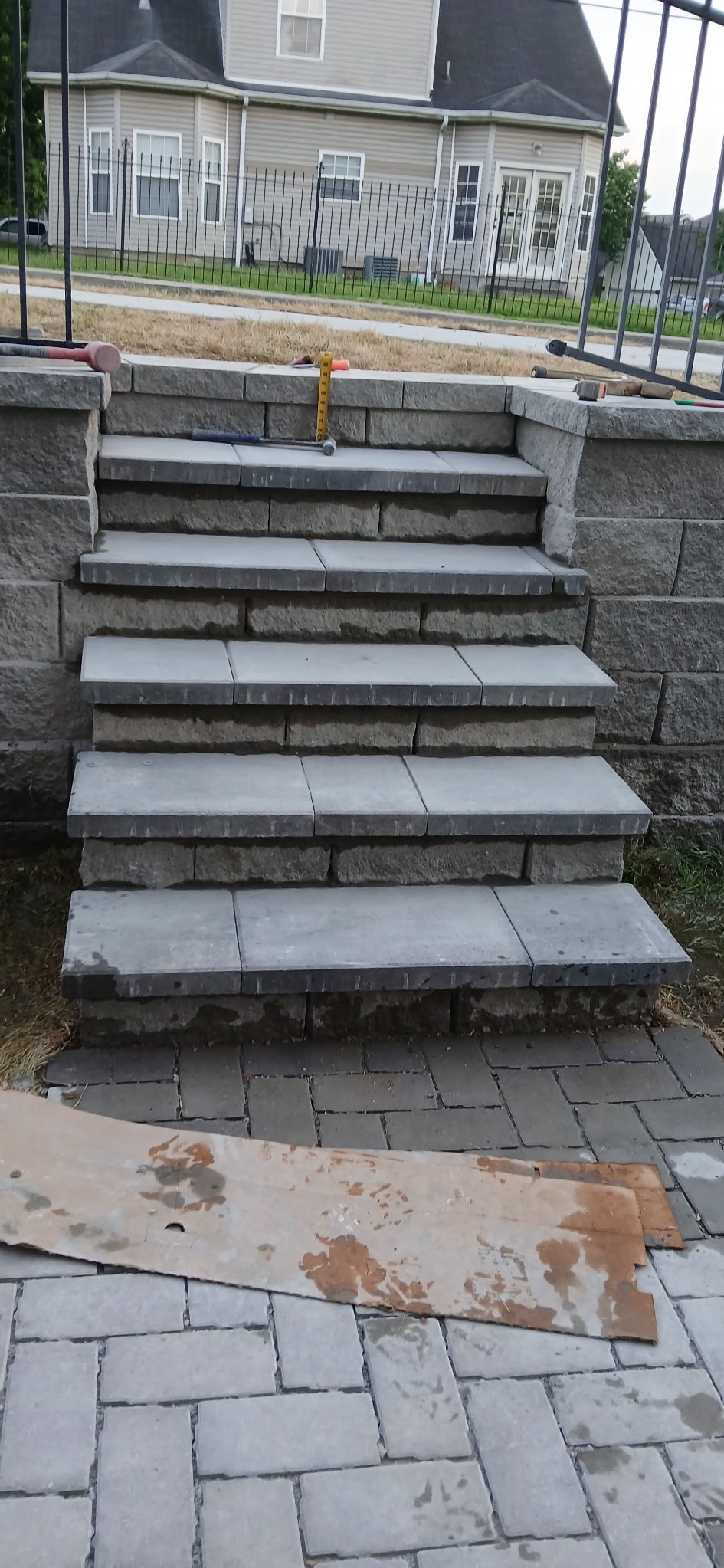 Construction site with stone steps being built, tools on top, and a wooden board on the paved ground in foreground.