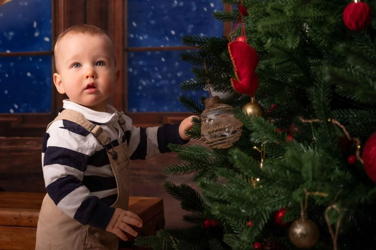 A young child decorating a Christmas tree with ornaments indoors at night.