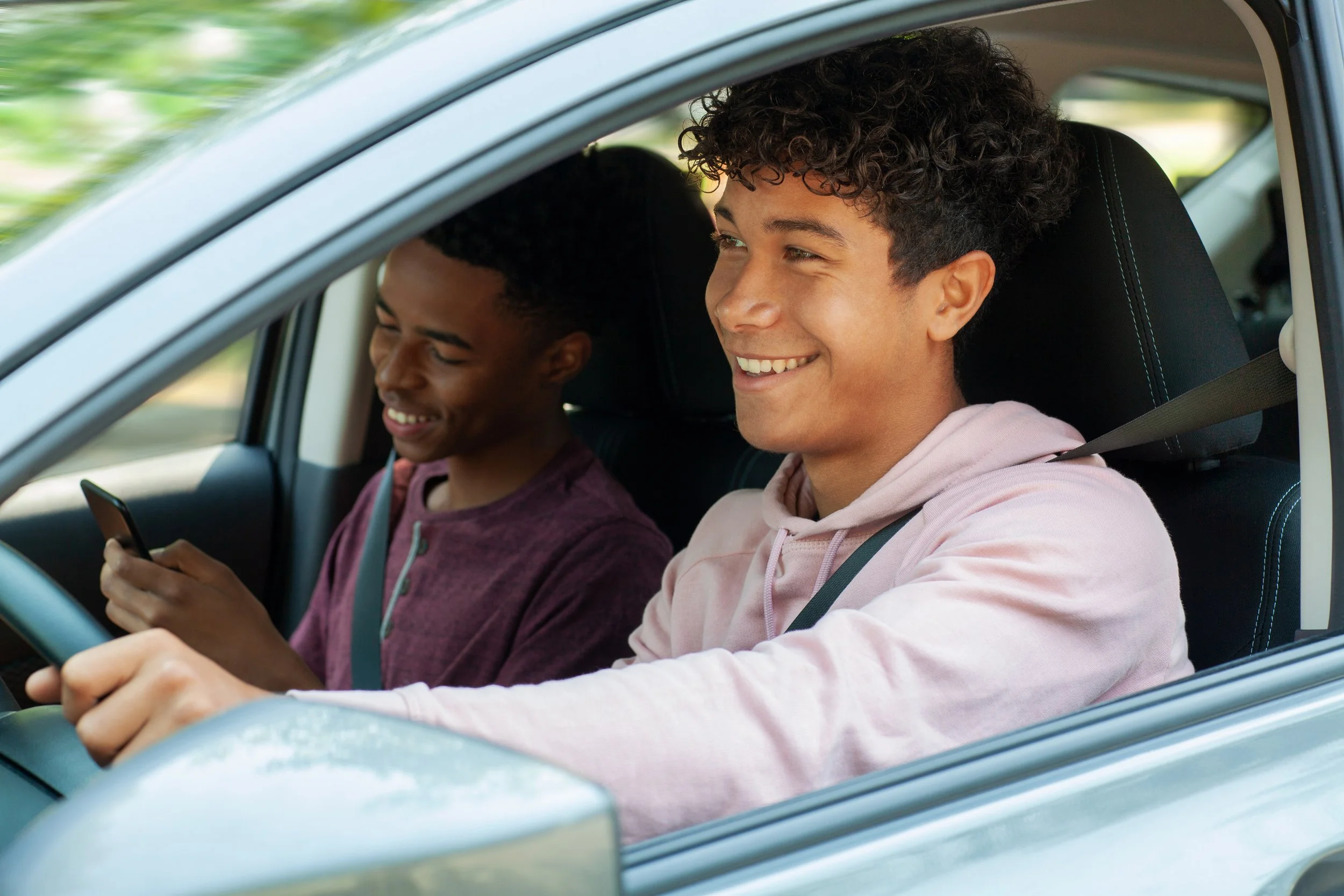 Teen boy driving safely in his car with a friend in the passenger seat