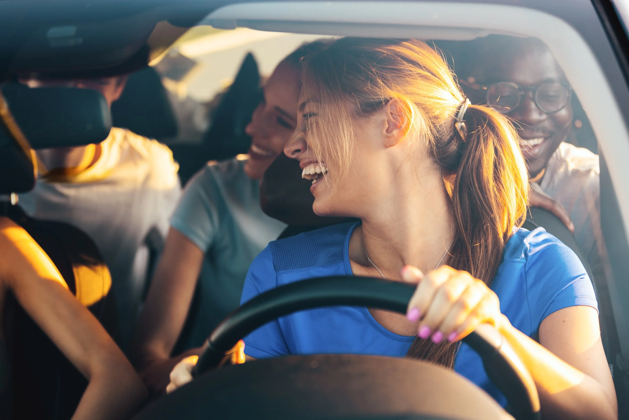 Four teens sitting in a car, smiling and laughing, with natural light coming through the window.