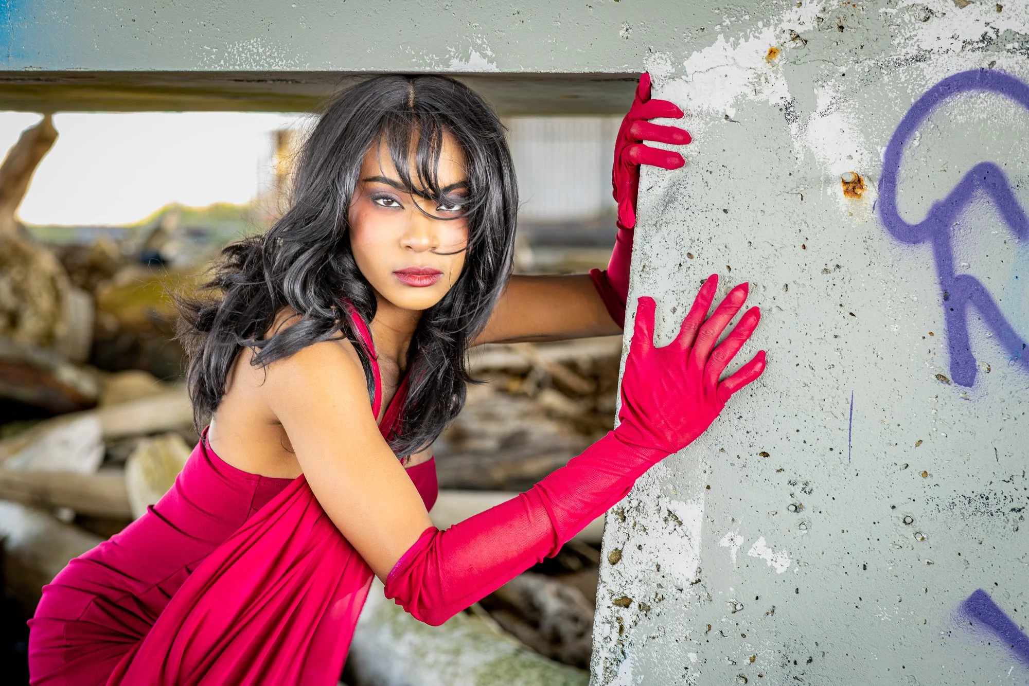 Woman in red dress and gloves gripping weathered concrete wall, intense direct gaze, editorial portrait Dumbarton Shoreline Trail