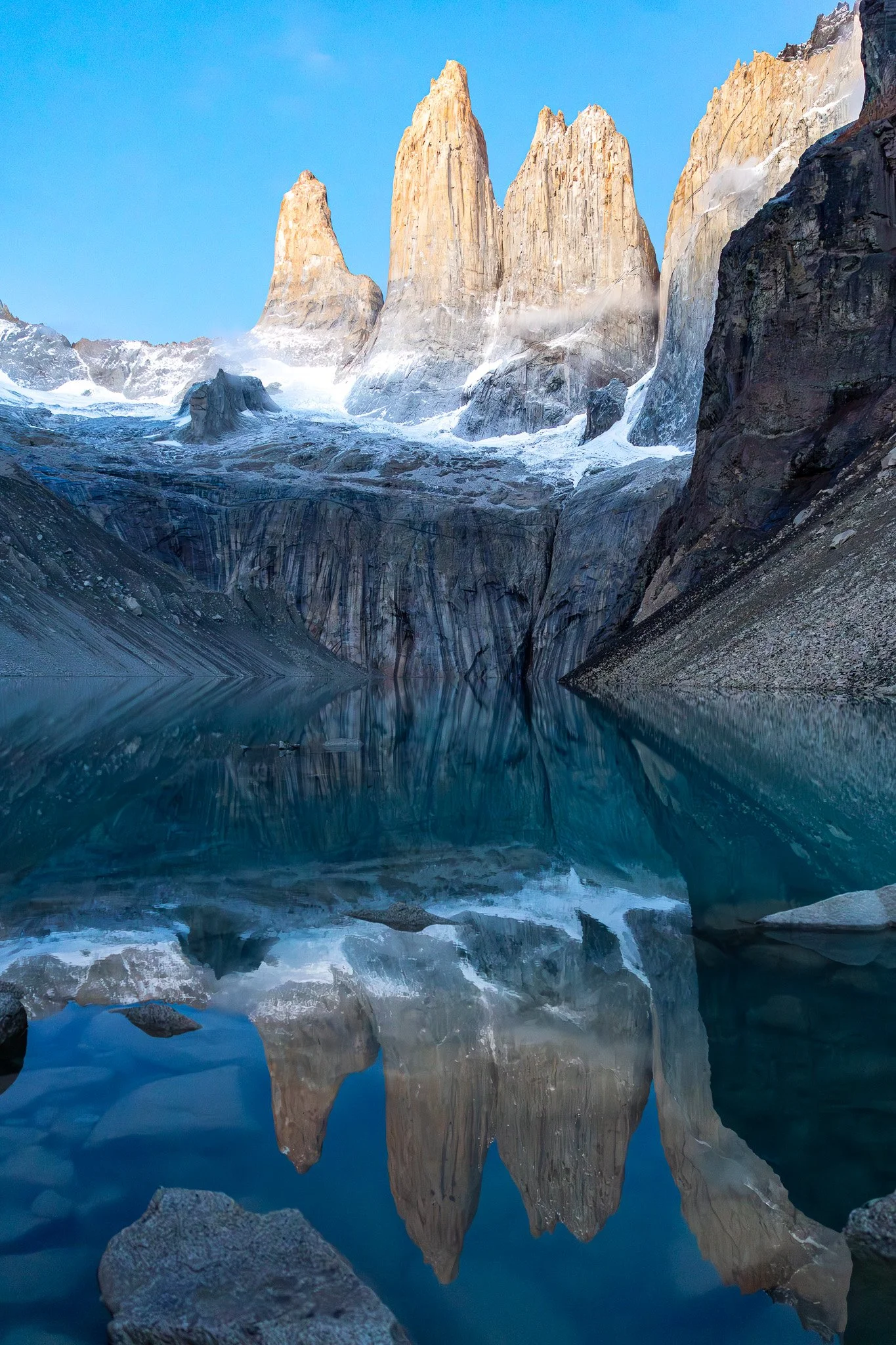 The three granite towers of Torres del Paine glowing amber-orange at sunrise perfectly reflected in still turquoise lagoon below, Torres Base