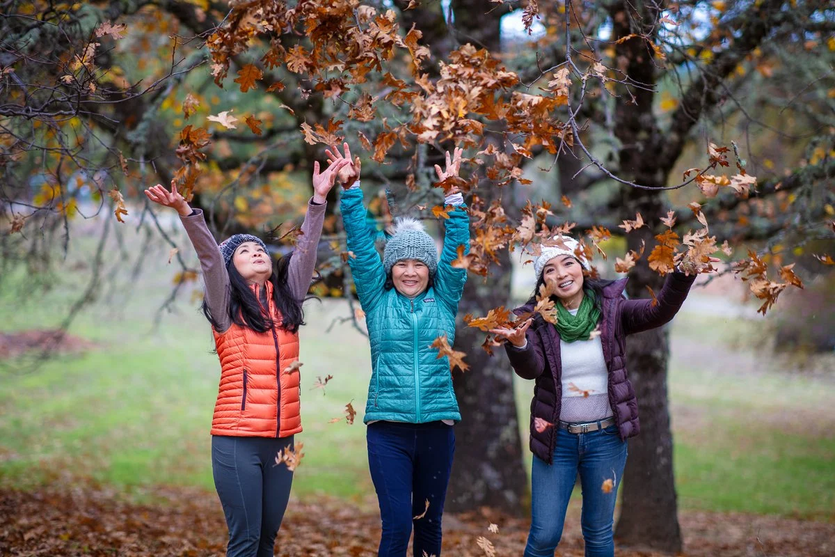 Three women throwing autumn leaves at a Bay Area family photography session in winter overcast light