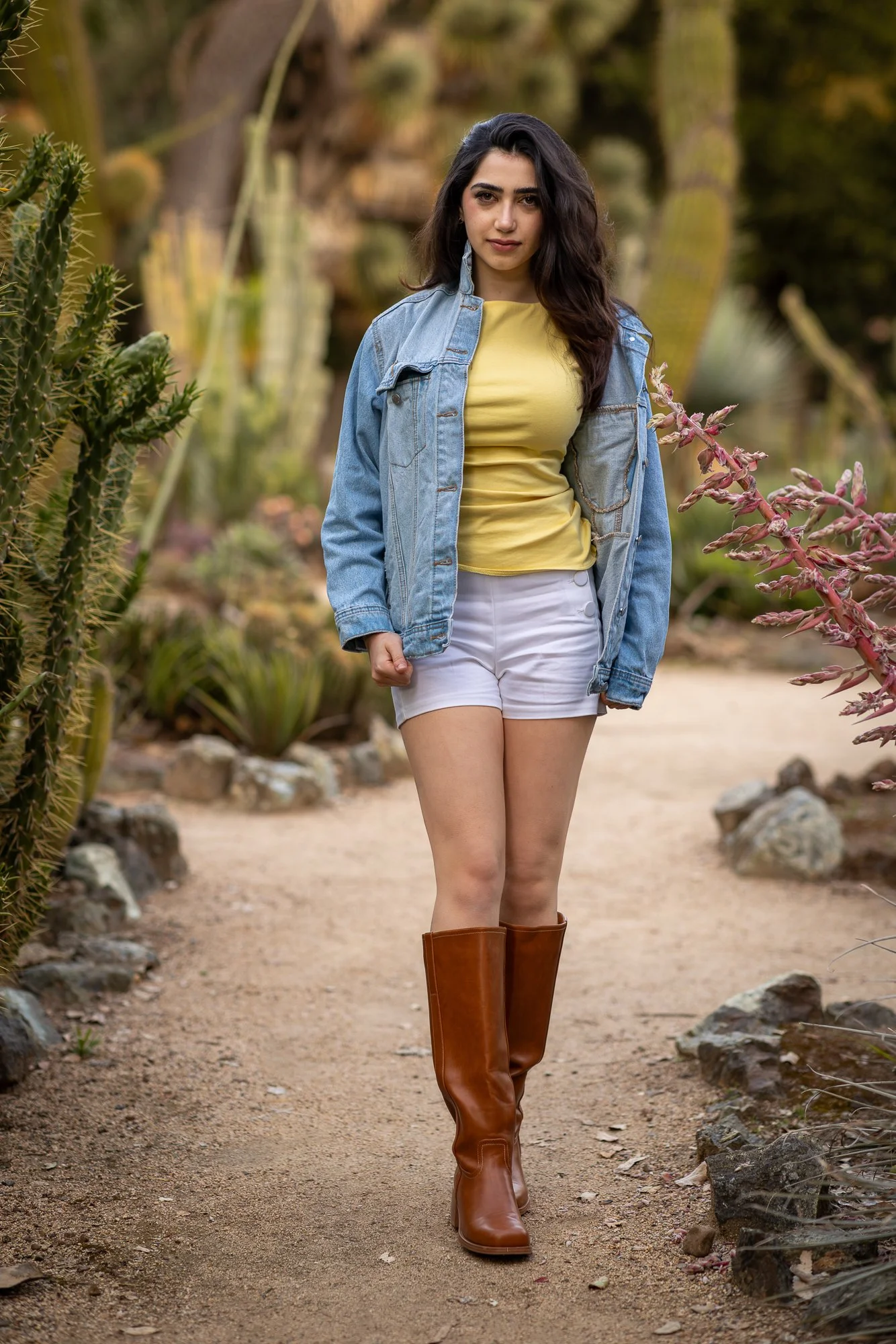 Woman in yellow top and denim jacket walking through cactus-lined path at Stanford Cactus Garden, natural light lifestyle photography Peninsula