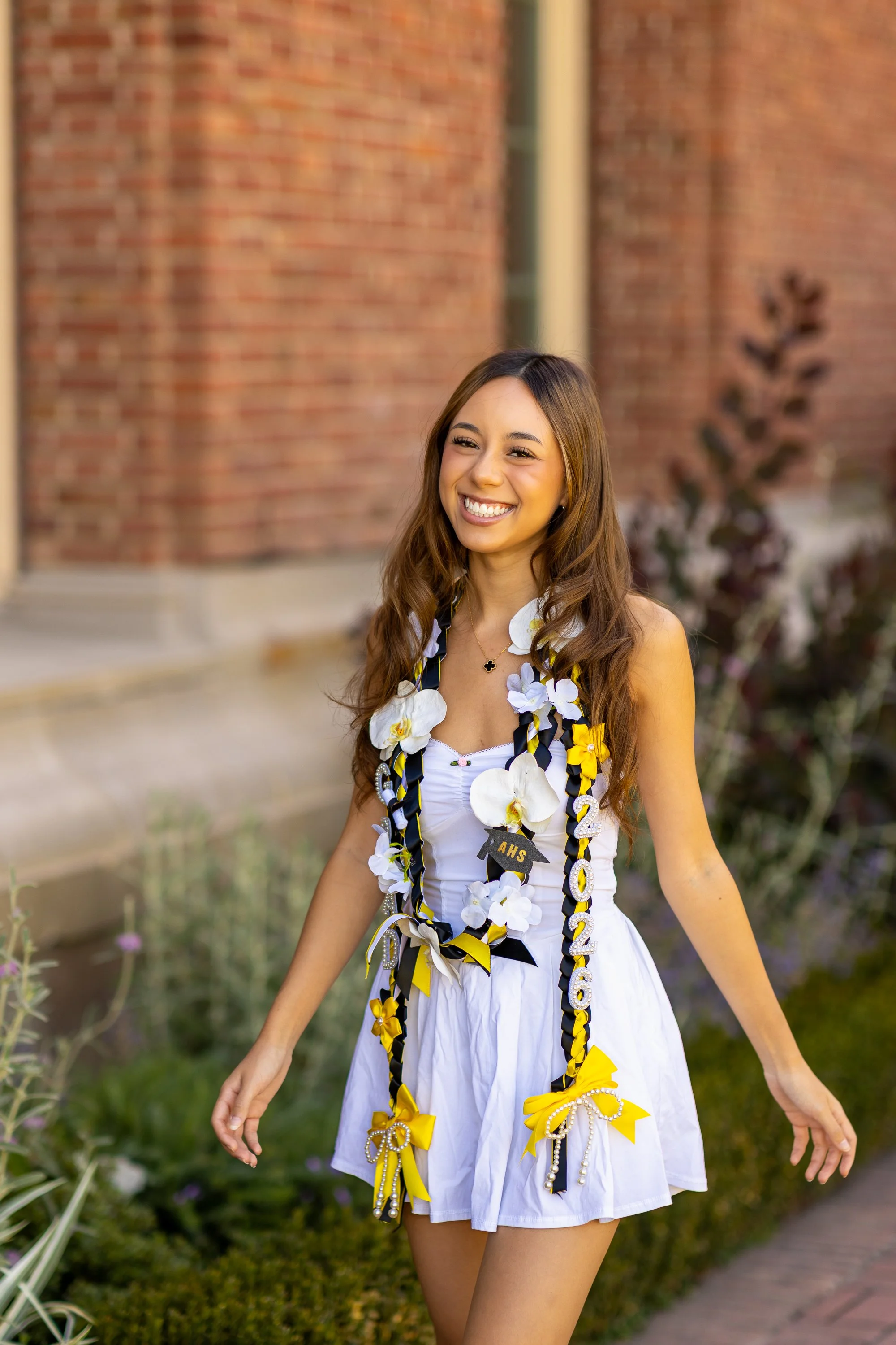 Laughing graduate with graduation lei against brick wall at Filoli garden