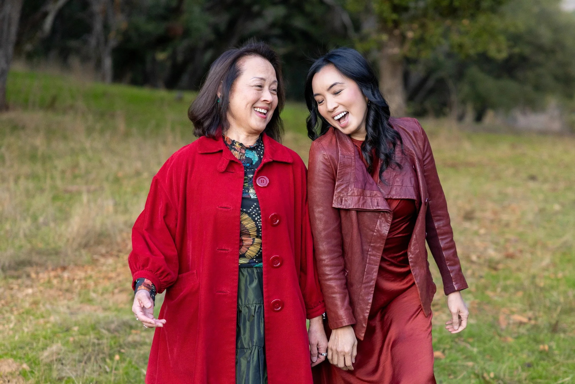 Two women in red coats walking and laughing together across meadow at Filoli Historic Garden Woodside California, lifestyle portrait photography