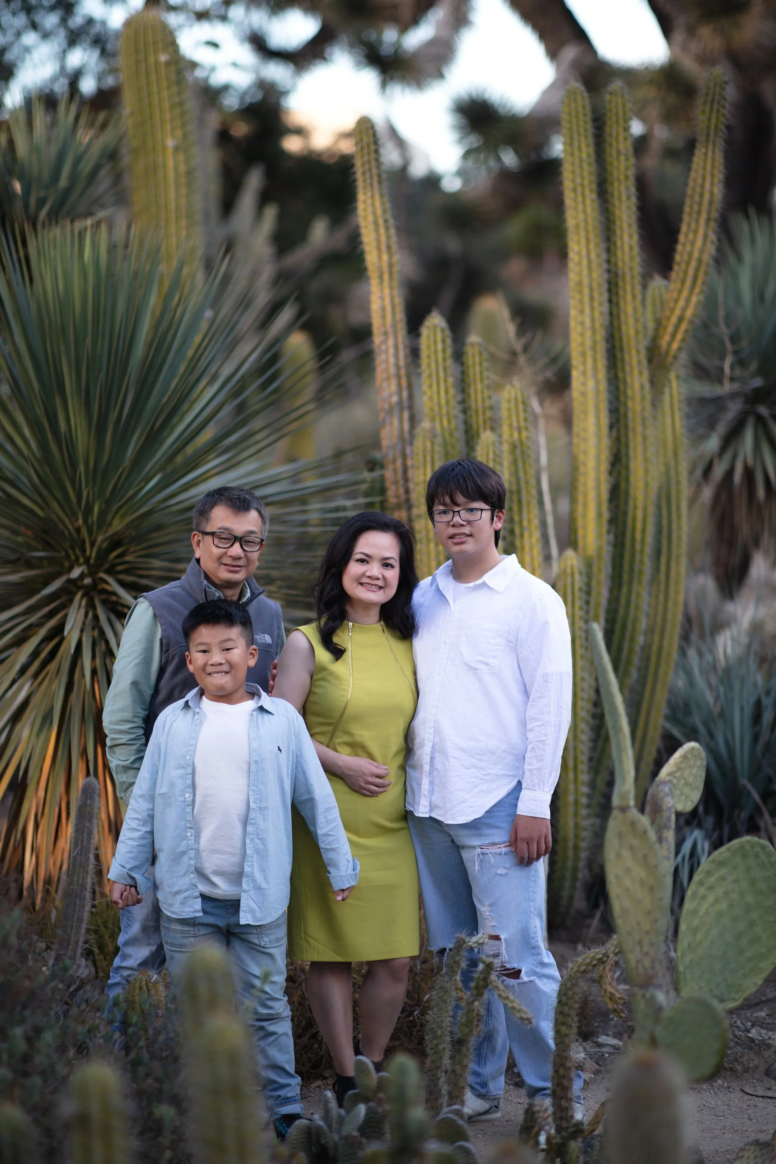 A family of five standing in a garden surrounded by large cacti and desert plants, smiling and posing for the photo.