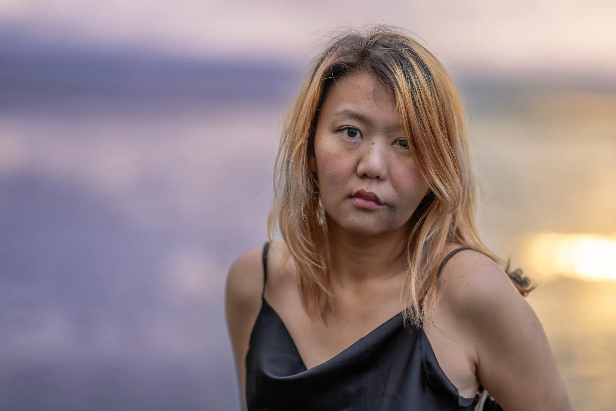 Woman in black silk dress seated on rock at sunset with golden San Francisco Bay reflection behind, Dumbarton Bridge photography Bay Area