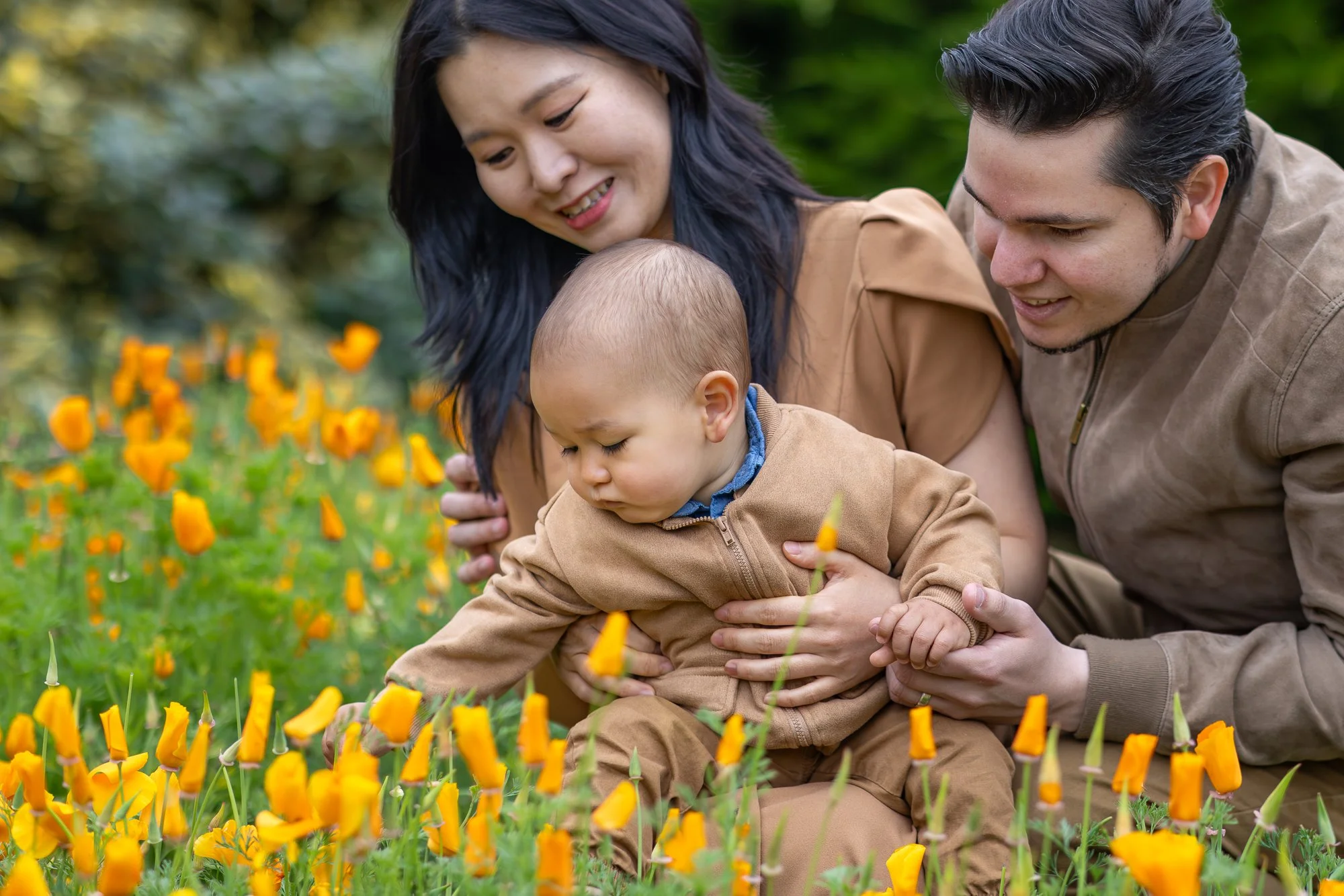 A family of three, a woman, a man, and a baby, sitting in a field of yellow flowers, smiling and enjoying nature.
