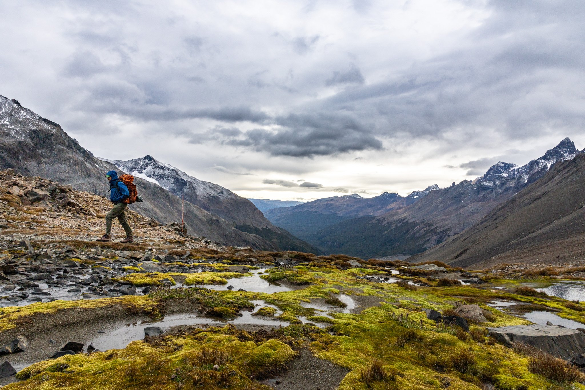 Hiker silhouetted on high plateau of Gardner Pass with chartreuse moss, glacial pools, and sweeping Patagonian valley behind, Torres del Paine