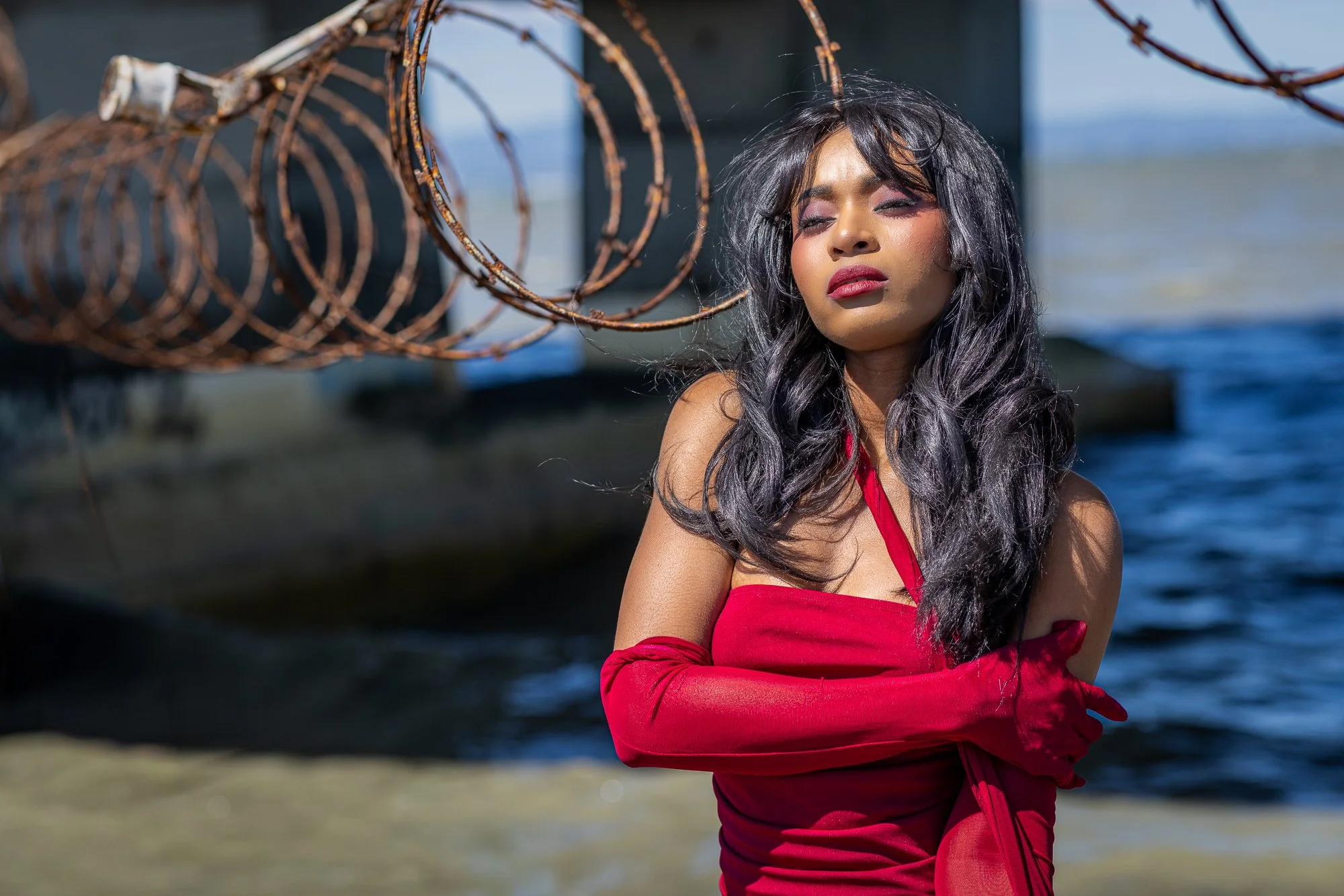 Editorial portrait with razor wire and bay water, woman in red dress, Dumbarton Bridge shoreline Newark California
