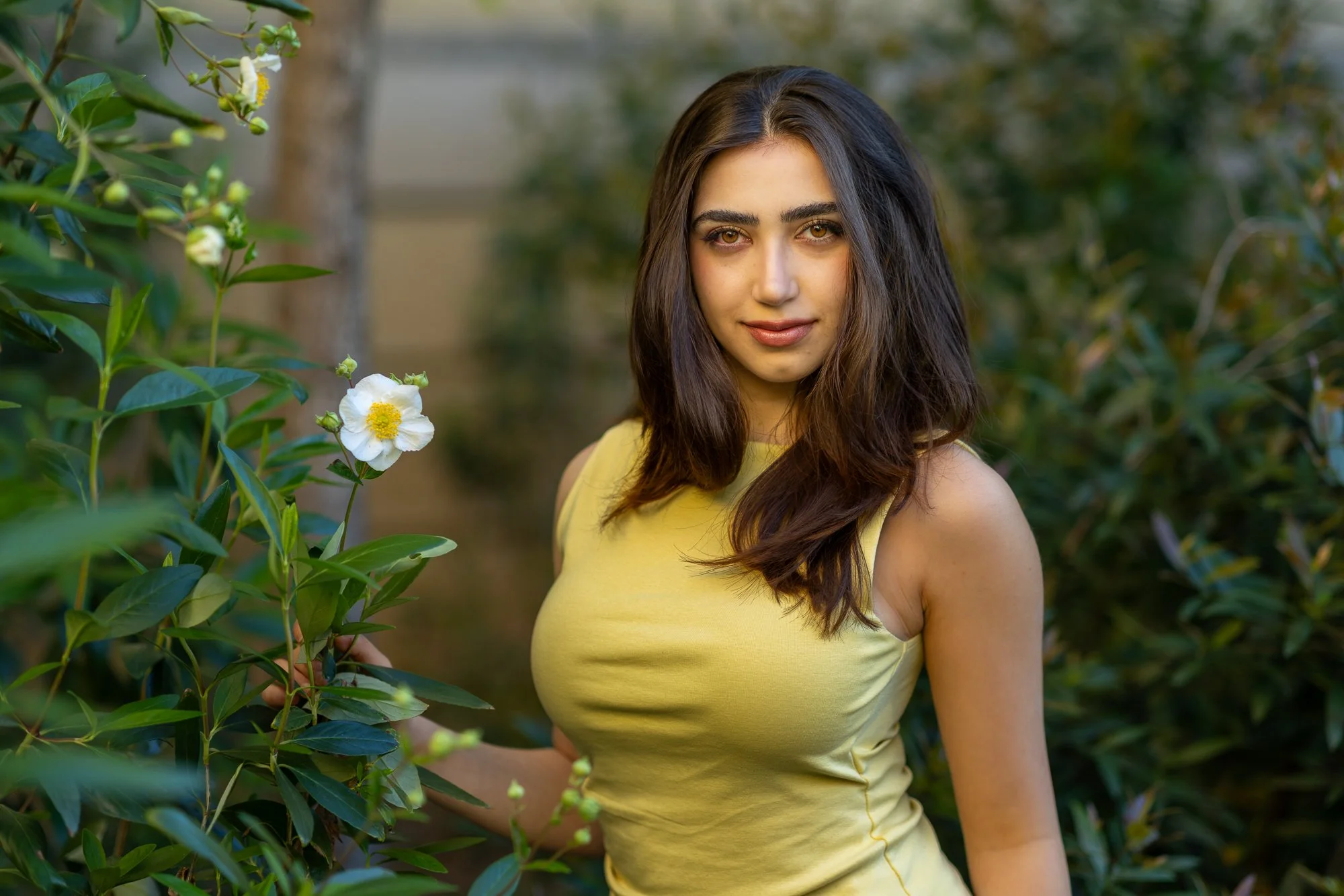 Woman in yellow top beside white flowering shrub at Stanford Cantor Arts Center garden, natural light lifestyle portrait Bay Area
