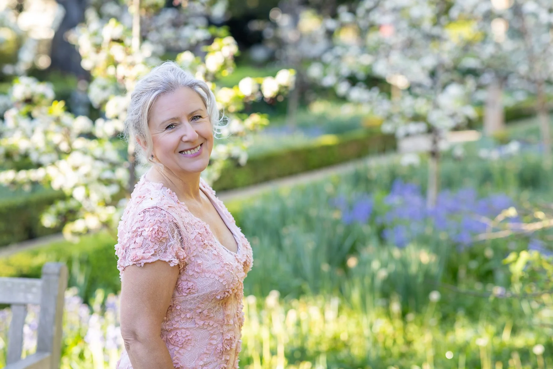Woman in blush pink dress laughing and smiling in spring orchard garden with apple blossom bokeh background, Elizabeth Gamble Garden Palo Alto