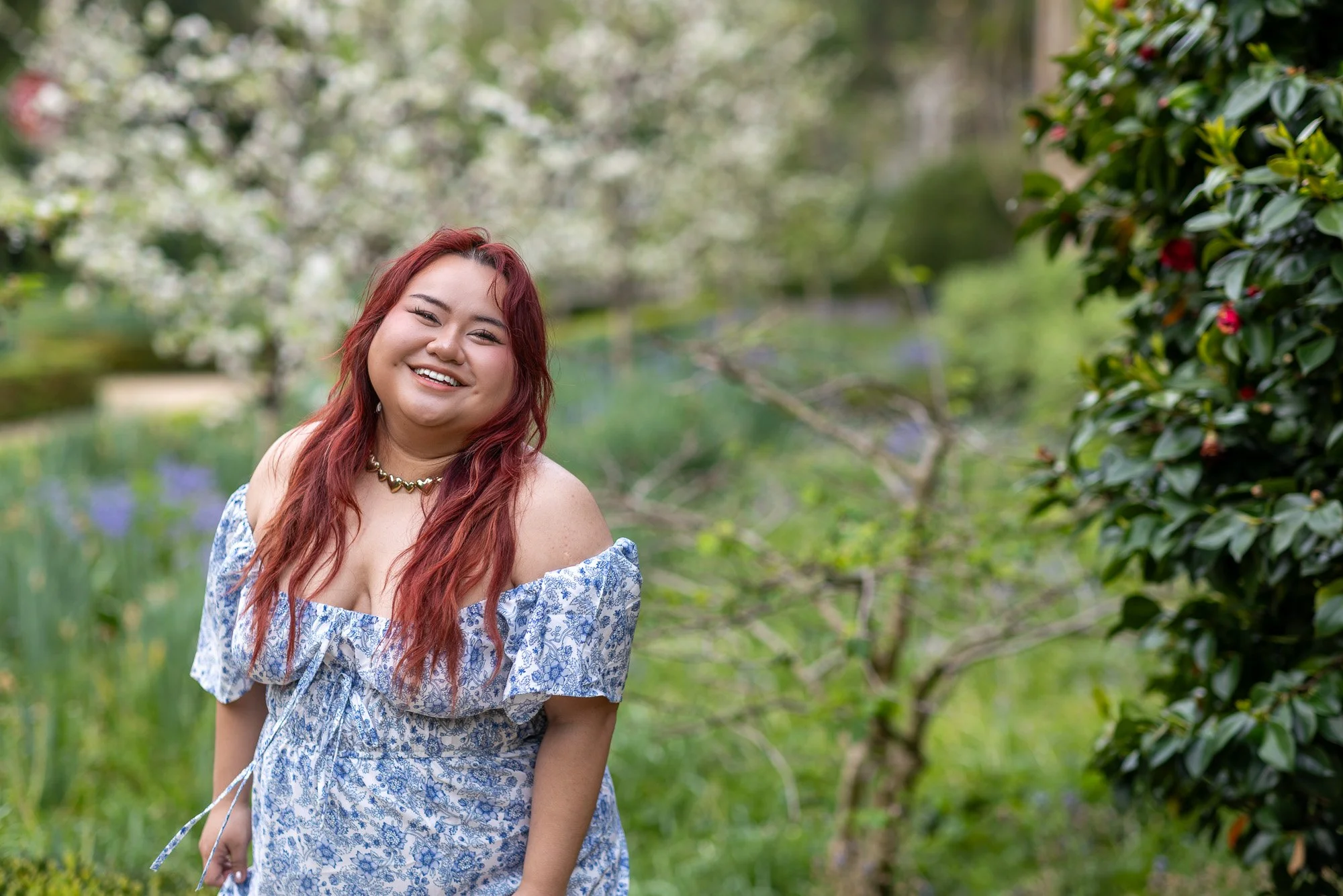 Woman in blue floral dress laughing and looking back over shoulder in spring orchard garden with apple blossom and camellia, Elizabeth Gamble Garden Palo Alto