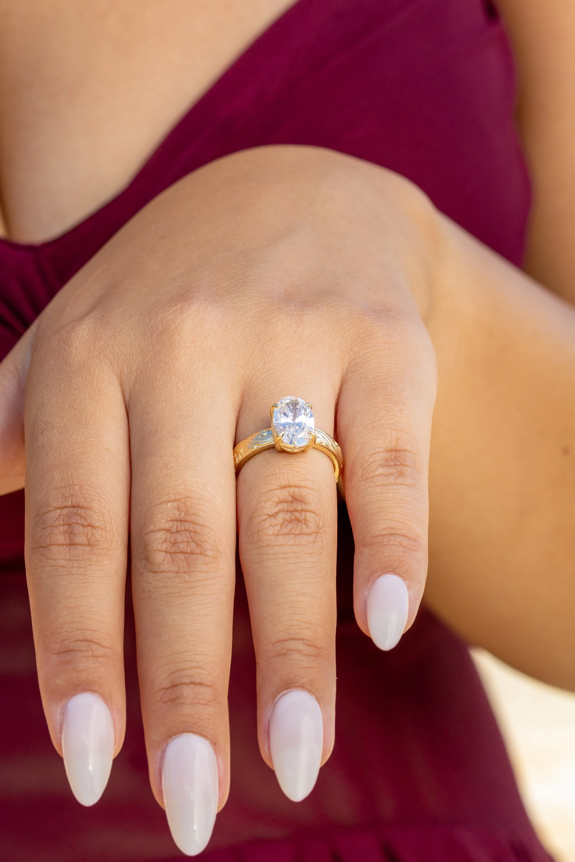 Close-up of a woman's hand with long, white, almond-shaped nails and a gold ring with a large diamond on her ring finger.