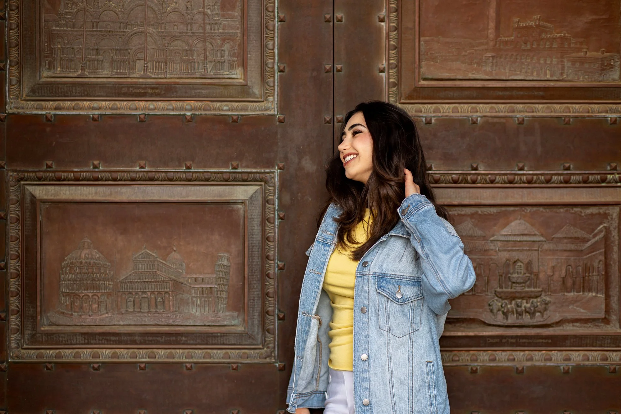 Woman laughing with hand in hair against ornate bronze relief doors at Stanford Cantor Arts Center, candid natural light portrait