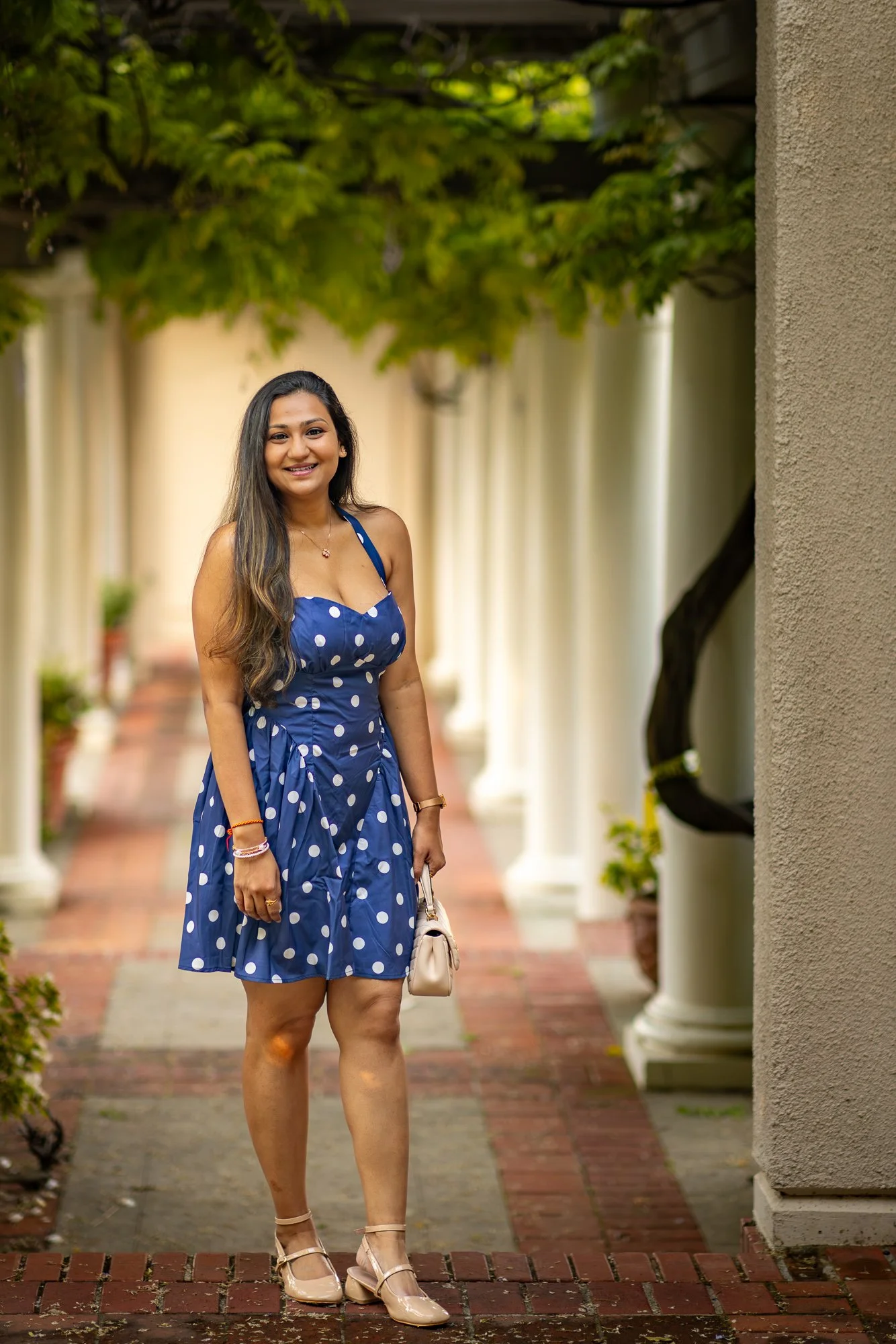 Woman in navy polka dot dress smiling beneath wisteria colonnade at Montalvo Arts Center Saratoga, natural light portrait session
