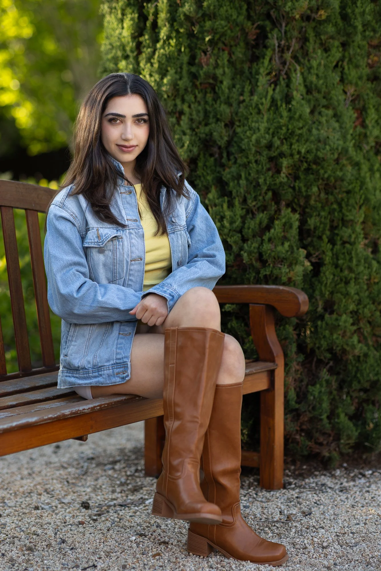 Woman in yellow top and denim jacket sitting on wooden bench between tall cypress trees, Stanford Cantor Arts Center, natural light portrait