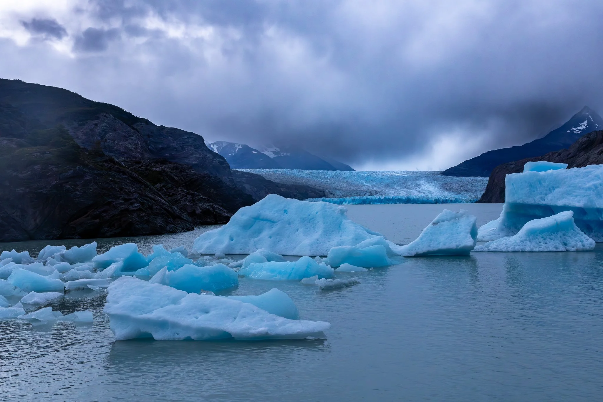 Blue icebergs on Lago Grey in early morning light under dark moody clouds with Glacier Grey face visible behind, Torres del Paine