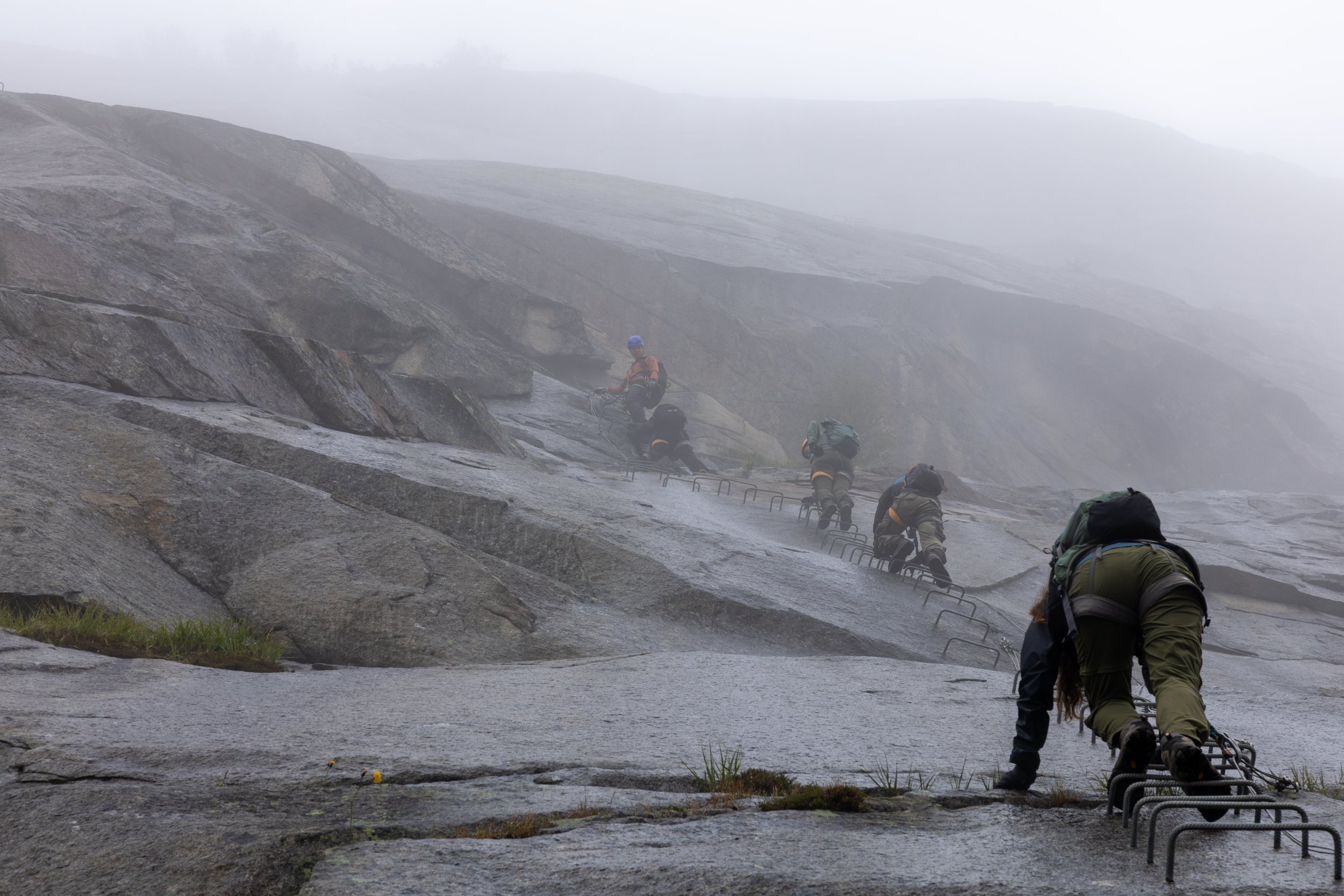 Climbers clipped to safety lines on a foggy mountain path preparing to climb.