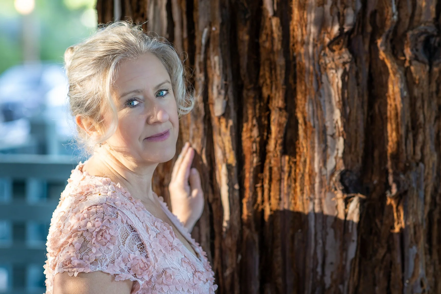 Close portrait of woman in pink dress leaning against redwood tree trunk with golden backlight, Bay Area outdoor portrait photographer