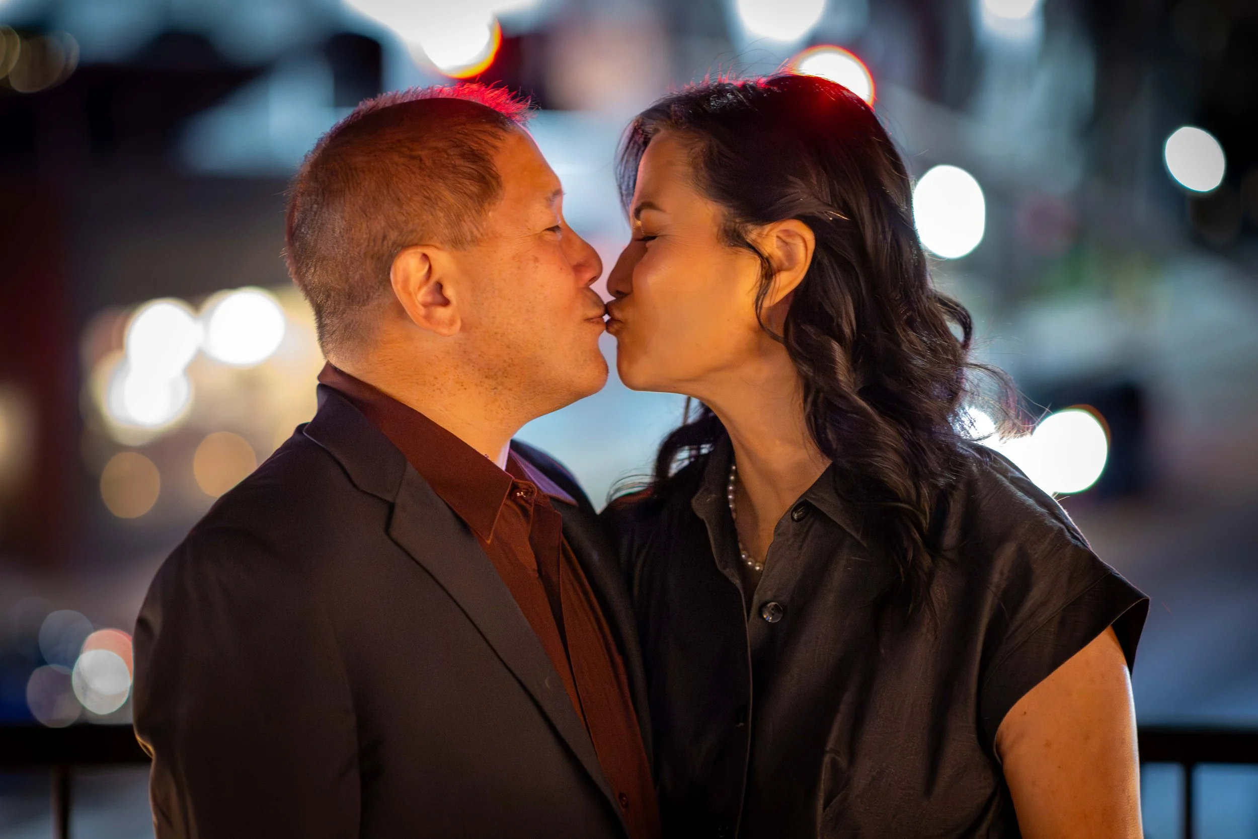 Romantic couple session outdoor night photography session in Willow Glen San Jose - a couple sharing a kiss at night with blurred city lights in the background.
