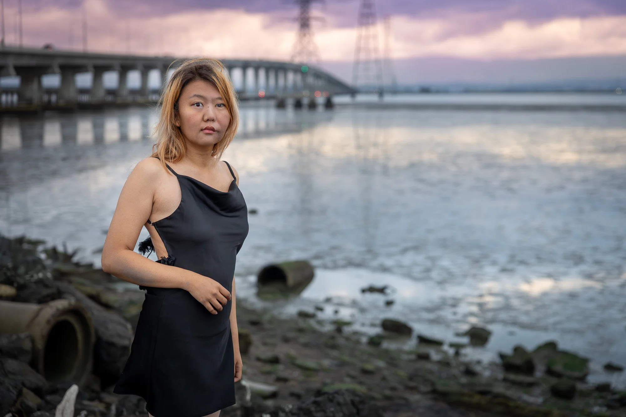 Woman in black dress standing beside rusted concrete pipe arch at bay shoreline, dusk sky, Dumbarton Bridge Shoreline Trail personal lifestyle photography