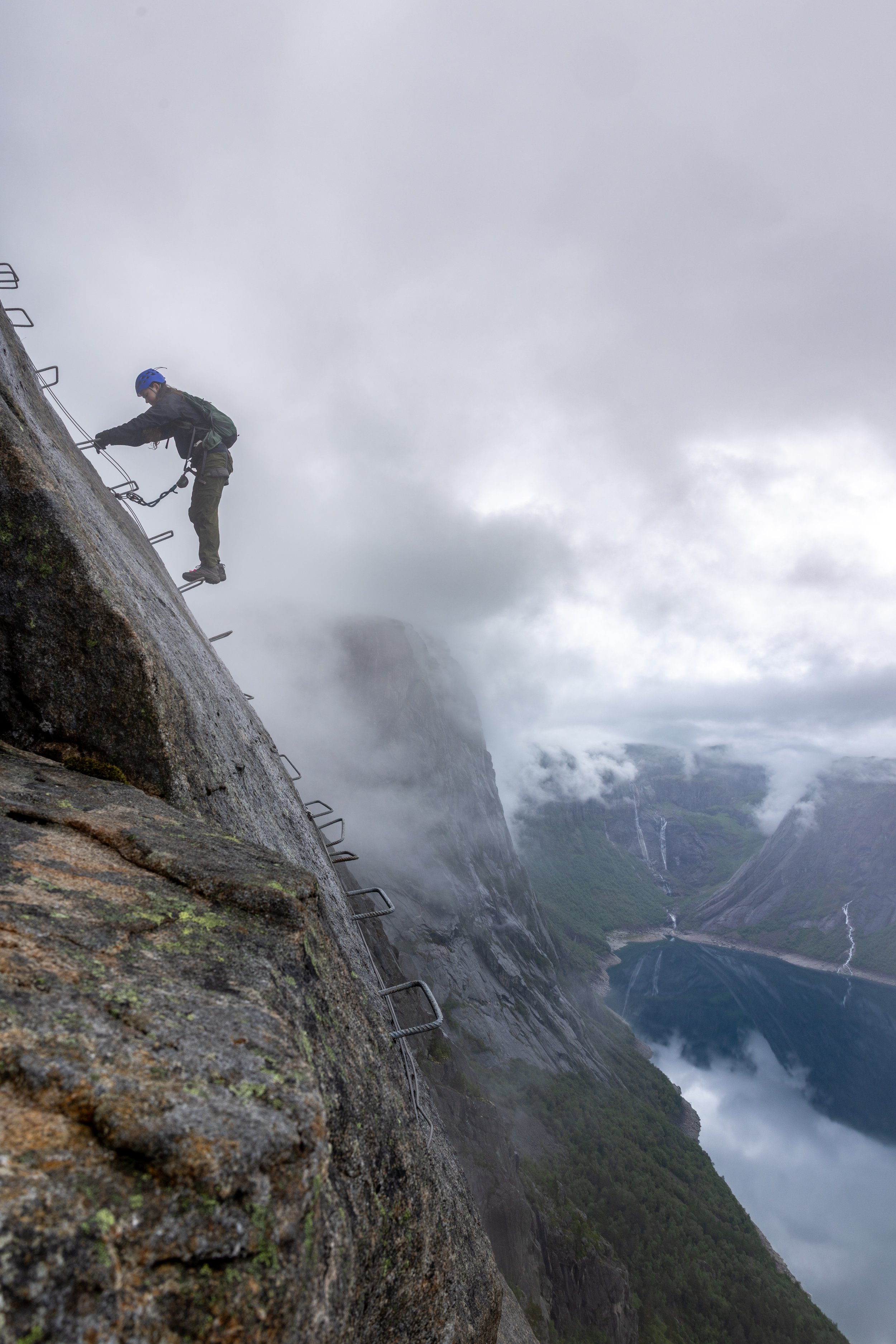 Mist swirling around climbers with a fjord briefly visible below