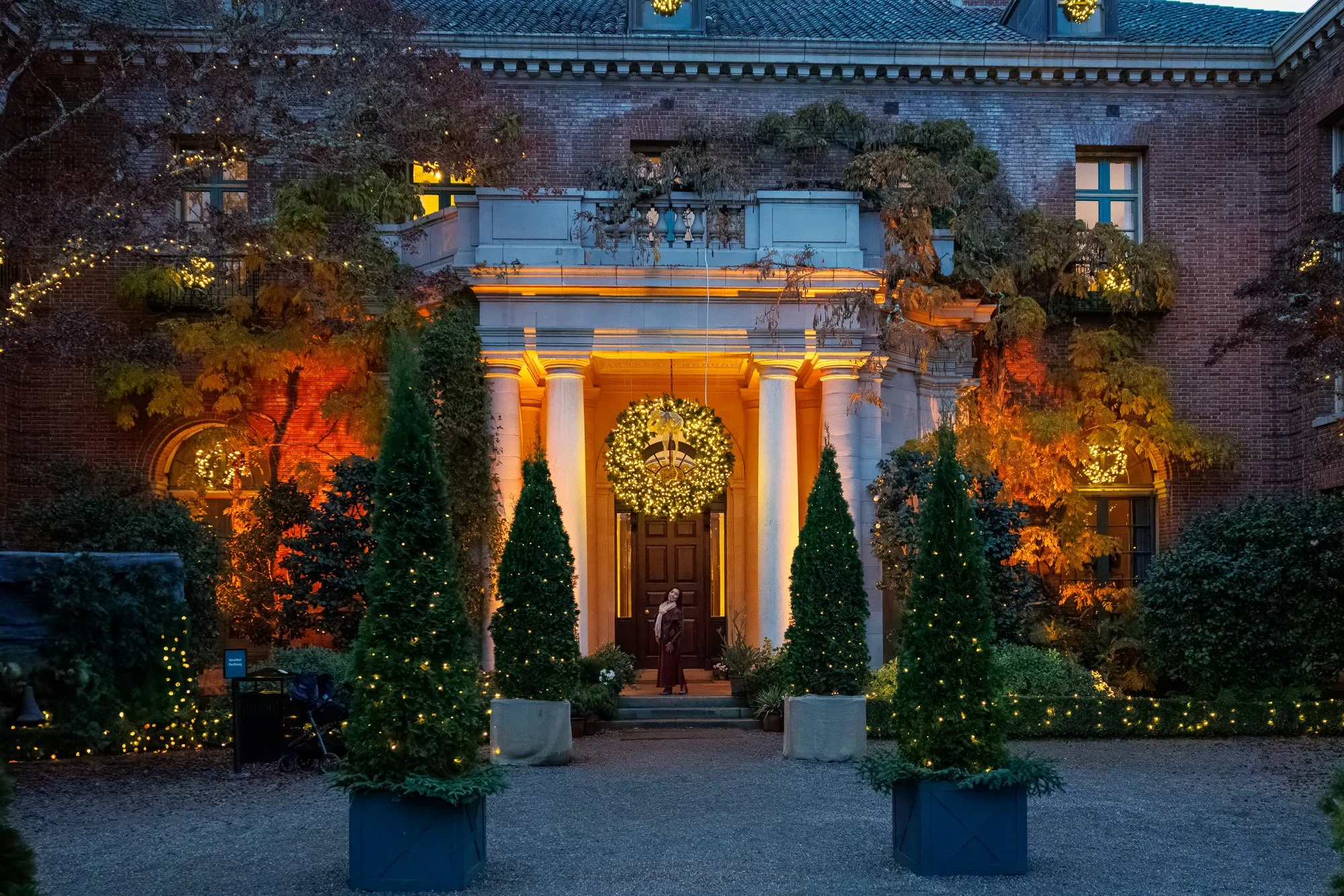 Woman standing in doorway of illuminated Filoli mansion with Christmas wreath and fairy lights, holiday portrait photography Bay Area