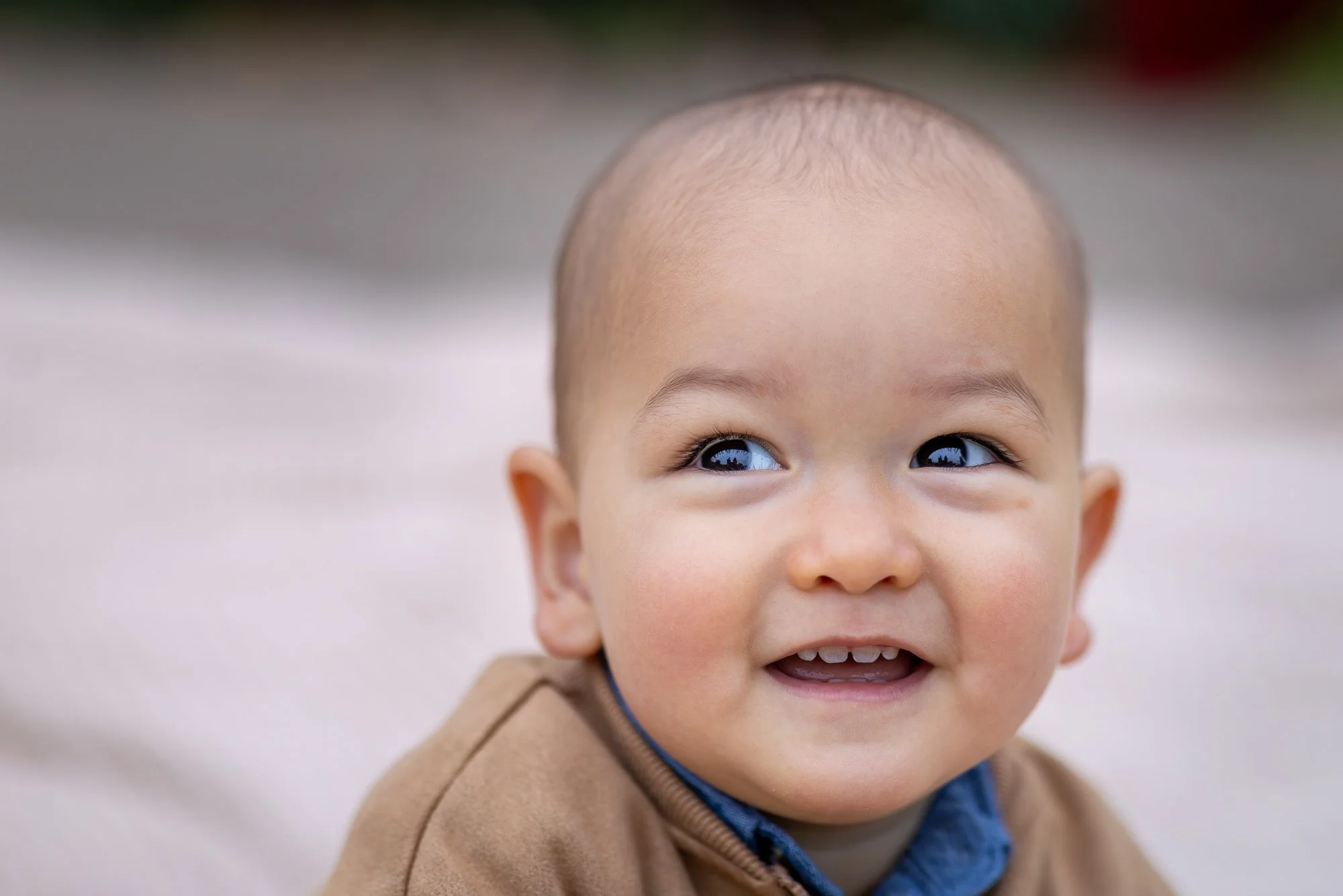 Close-up of a young child smiling outdoors, with a blurred background.