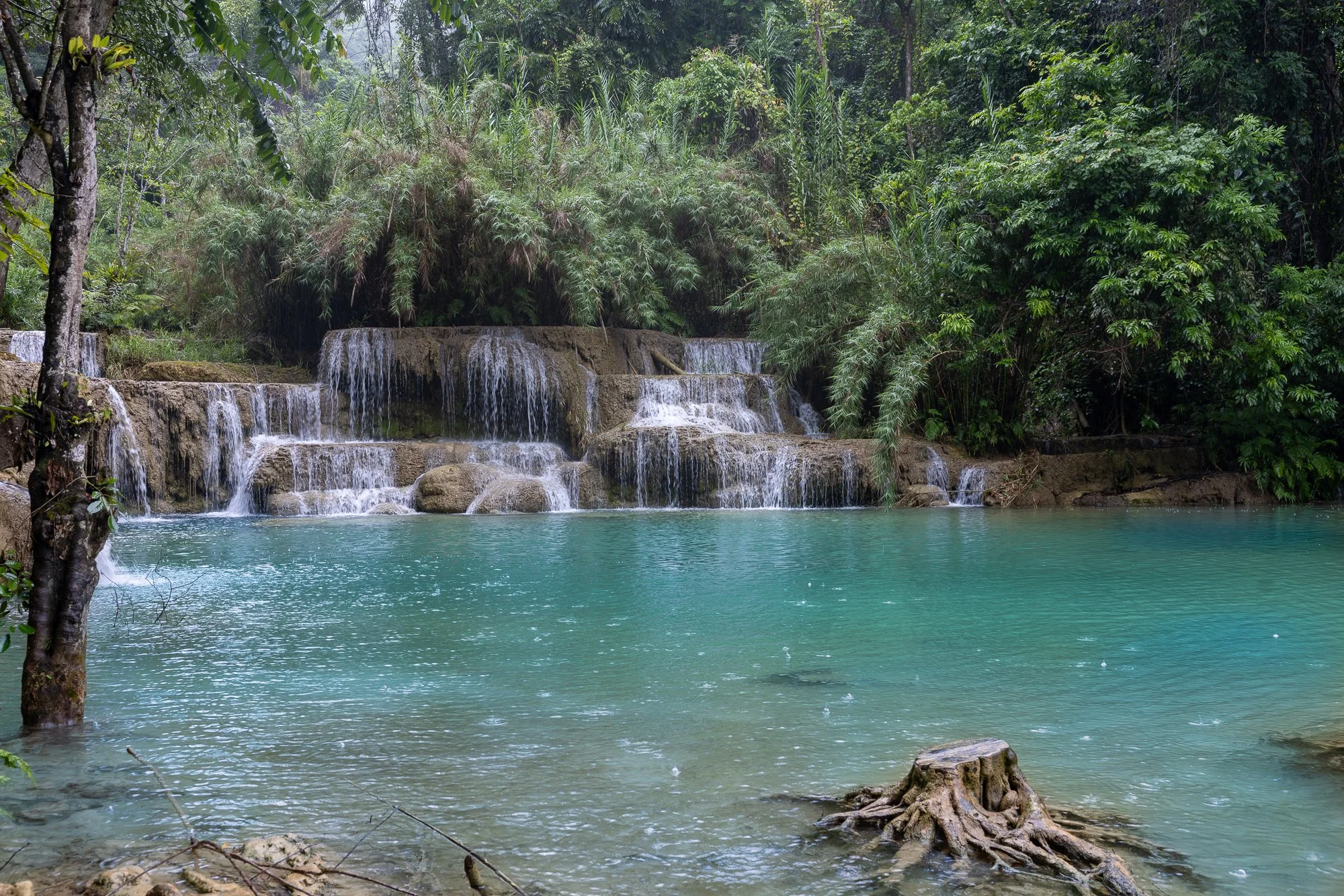 Turquoise travertine pool and tiered cascade in rain at Kuang Si Falls near Luang Prabang