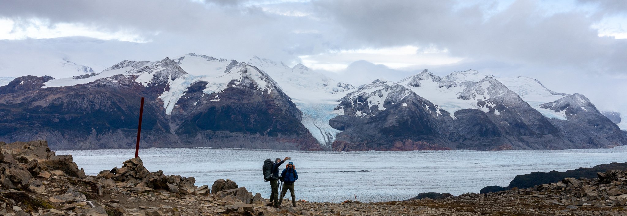 Two hikers taking a selfie on Gardner Pass above Glacier Grey with vast blue ice field and snow-capped peaks stretching behind, Torres del Paine