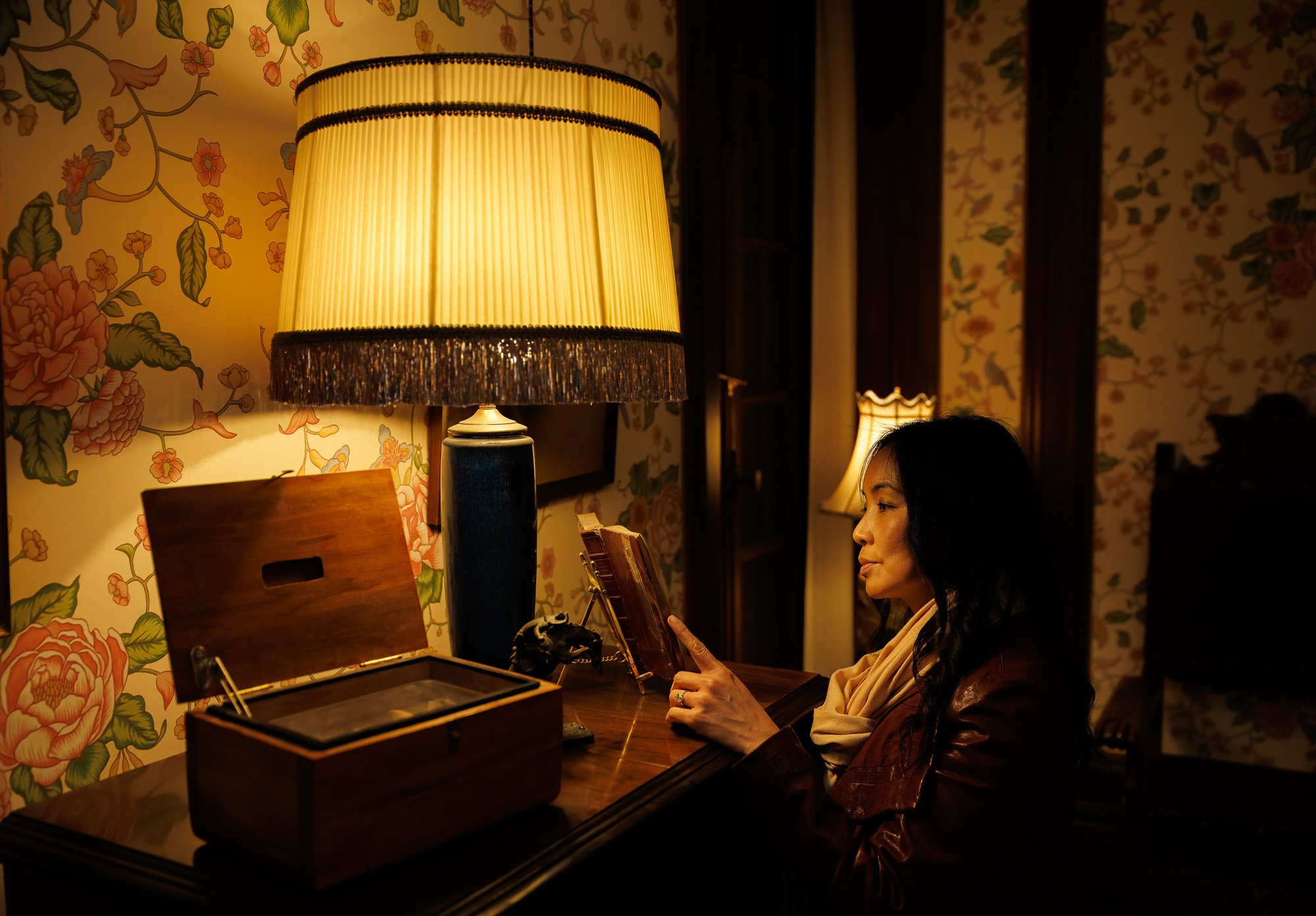 Woman sitting at antique writing desk beside vintage lamp with hand-painted floral wallpaper, interior portrait photography Filoli Historic House