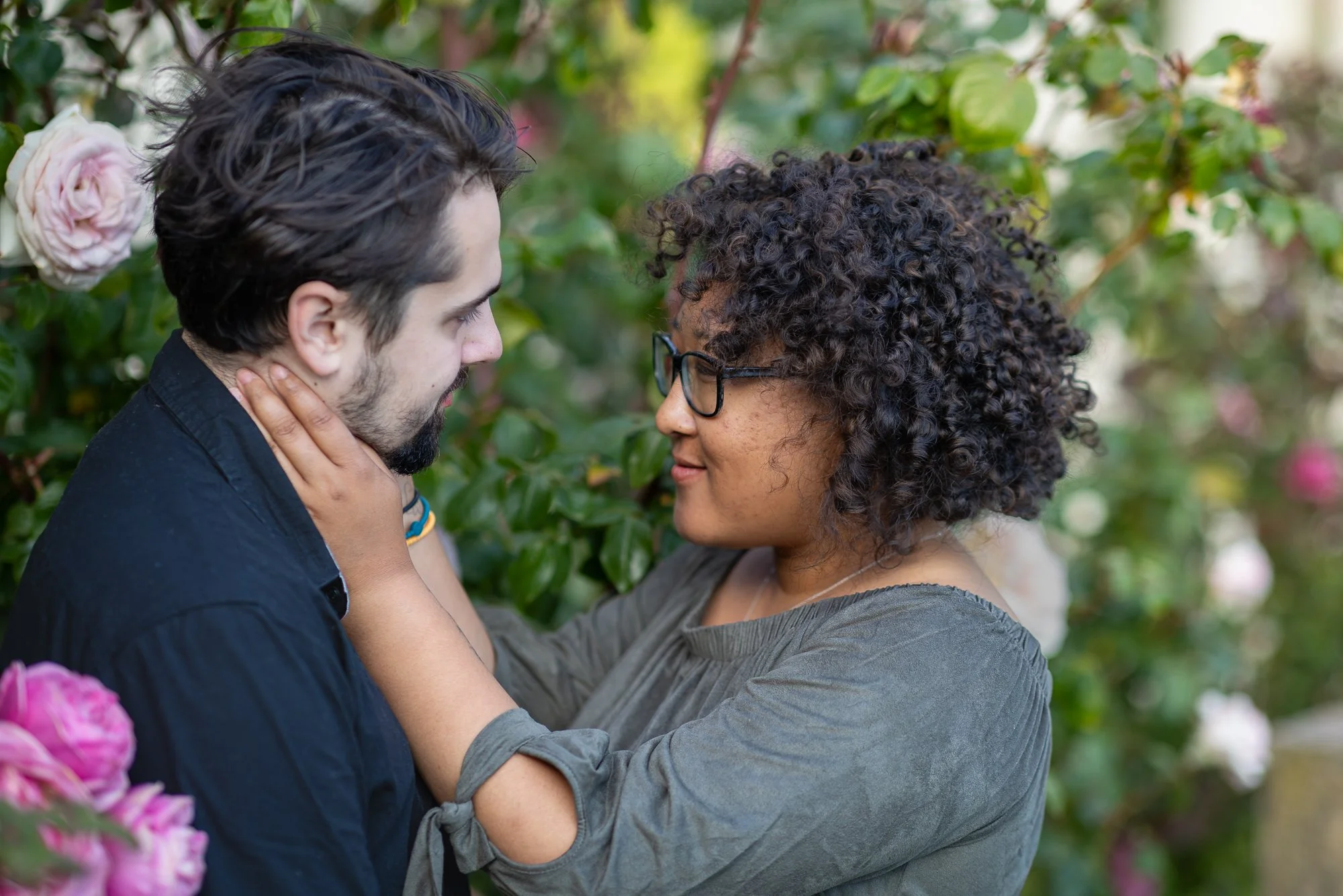 A couple sharing a close and intimate moment outdoors surrounded by pink and white roses.