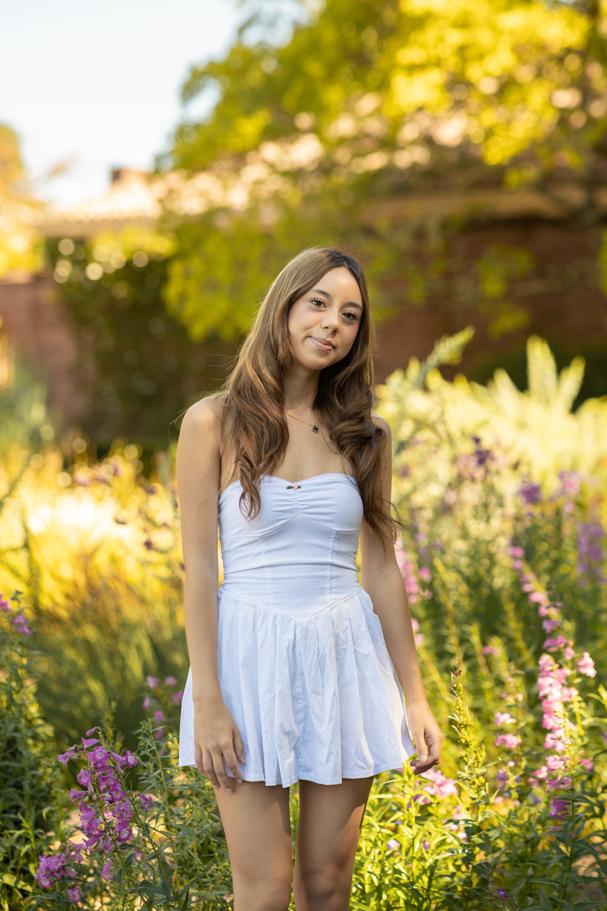 Senior in white dress standing in backlit garden border at Filoli, Bay Area