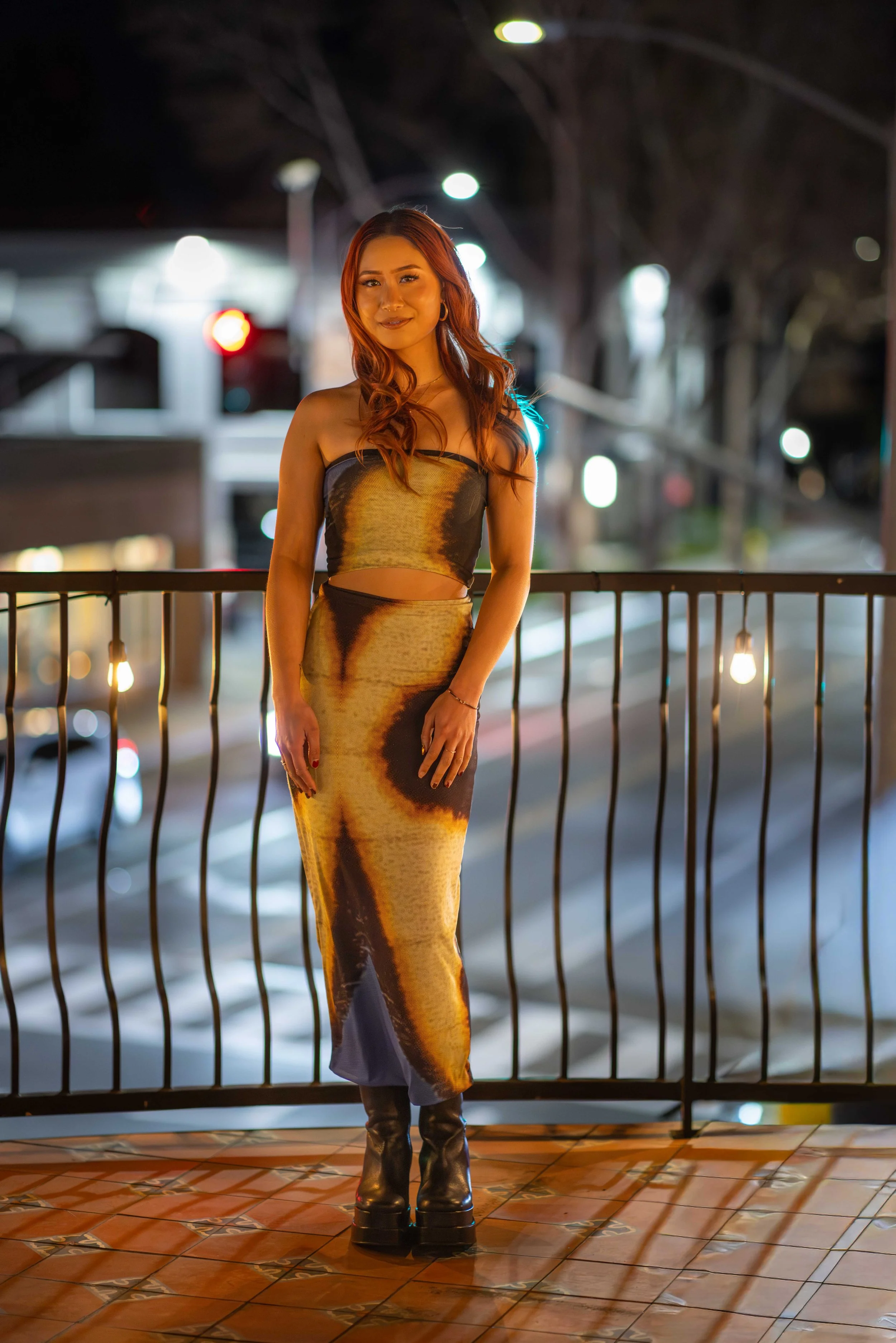 Personal branding photography session Willow Glen Bay Area - woman with long red hair in a dress with an abstract pattern standing on a balcony at night.