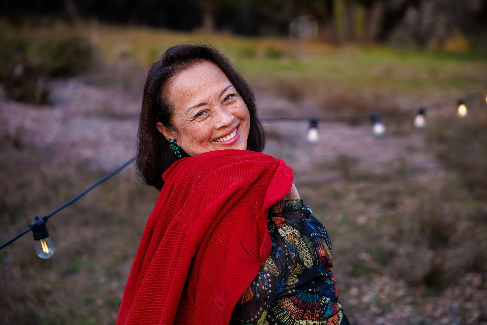 Woman in red jacket smiling and looking back over shoulder with string lights bokeh background at Filoli holiday lights event Woodside California