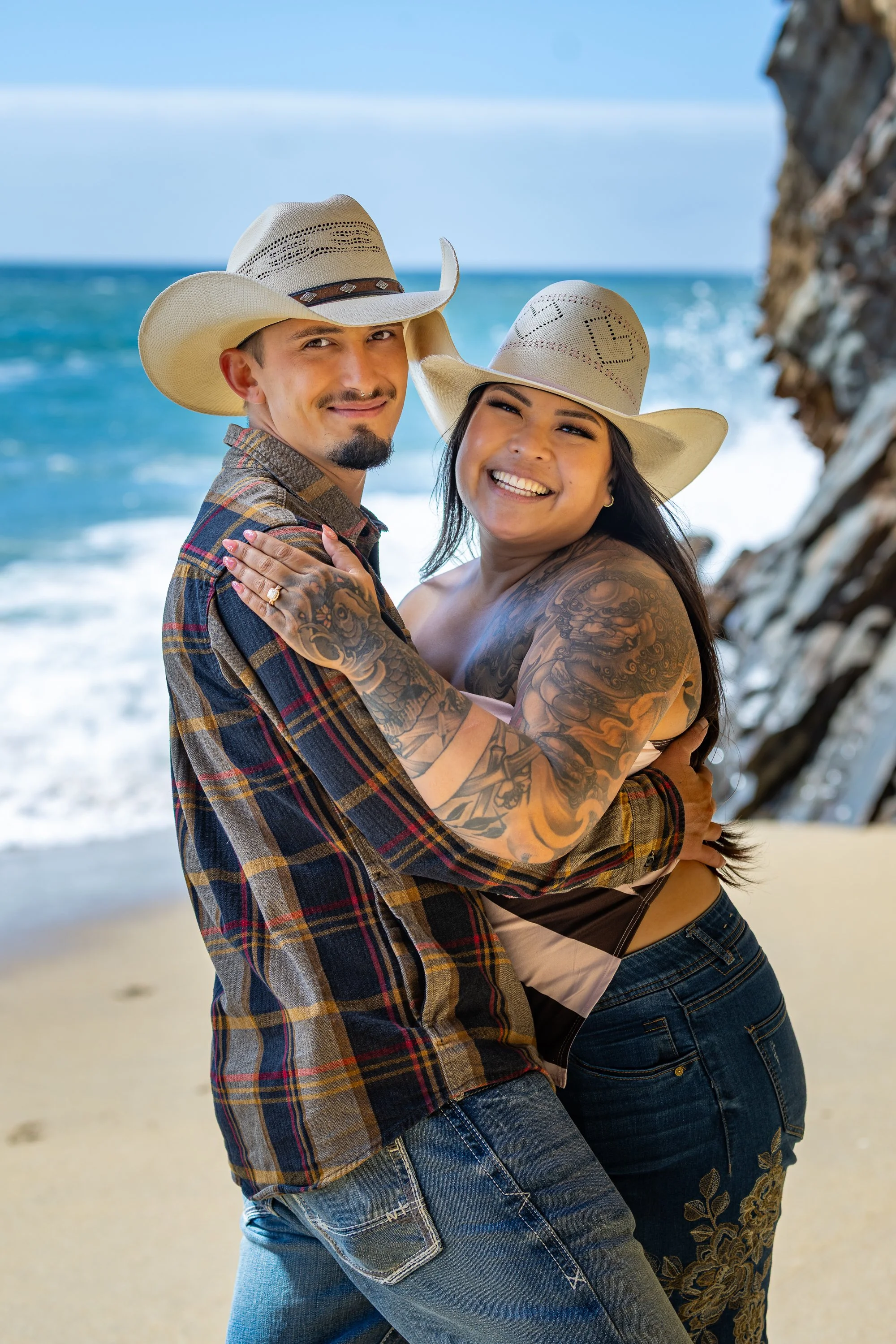 Engaged couple in cowboy hats laughing at Panther Beach, Santa Cruz