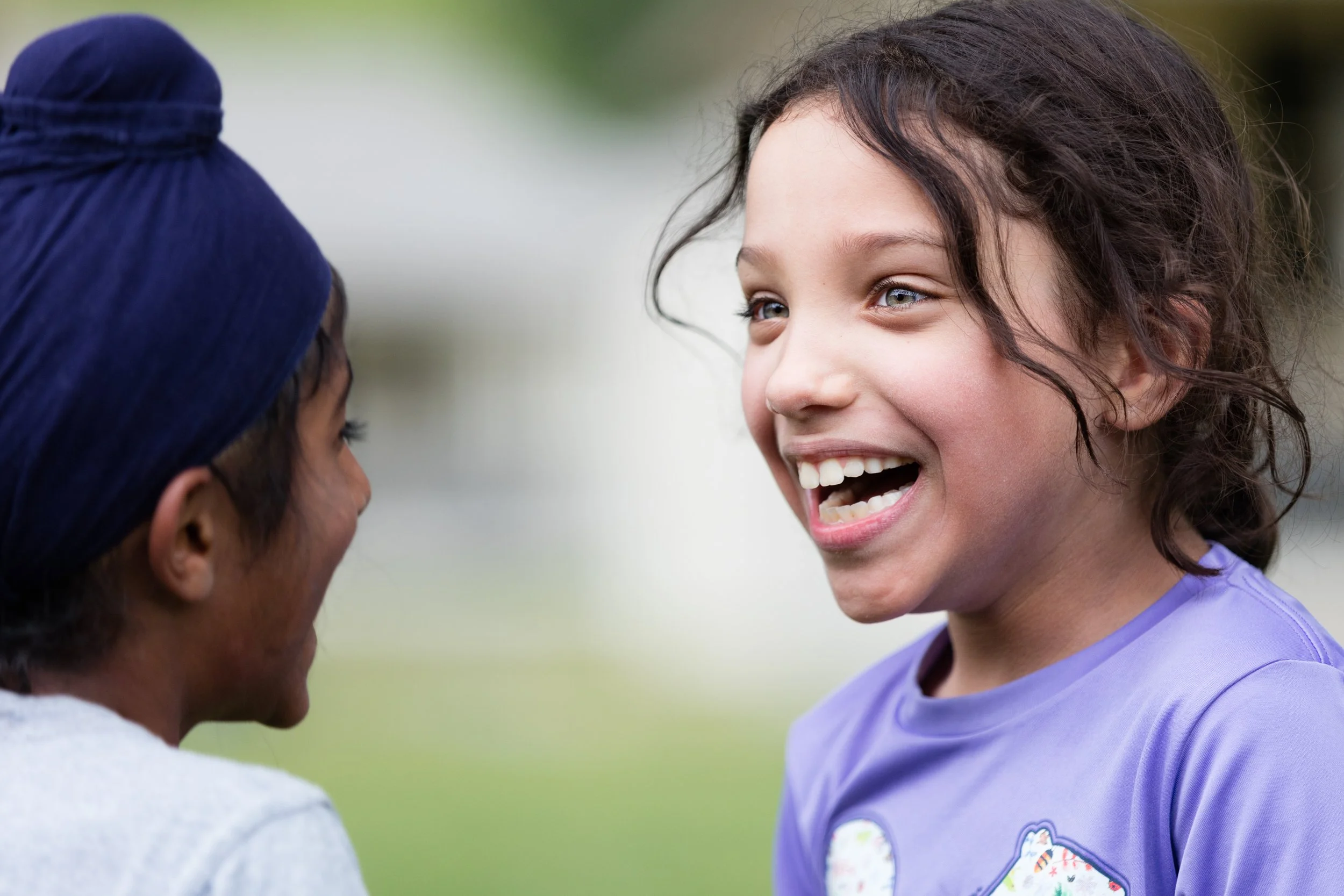 Bay Area photography session - Two children smiling and facing each other outdoors, one with dark curly hair and the other with a dark blue turban.