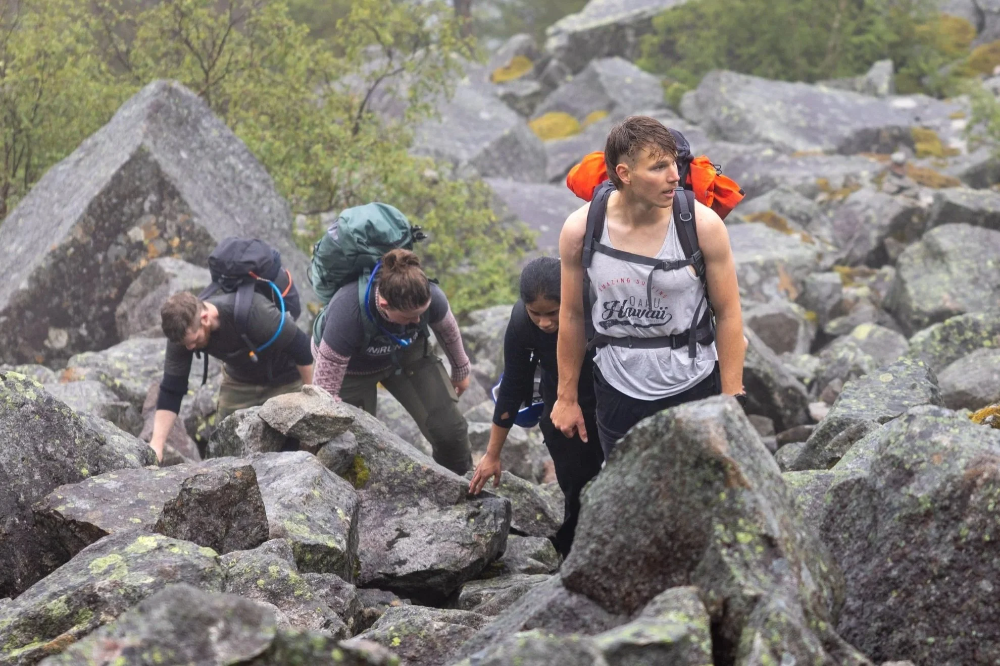 Hikers ascending a rocky trail in steady rain with wet jackets and backpacks.