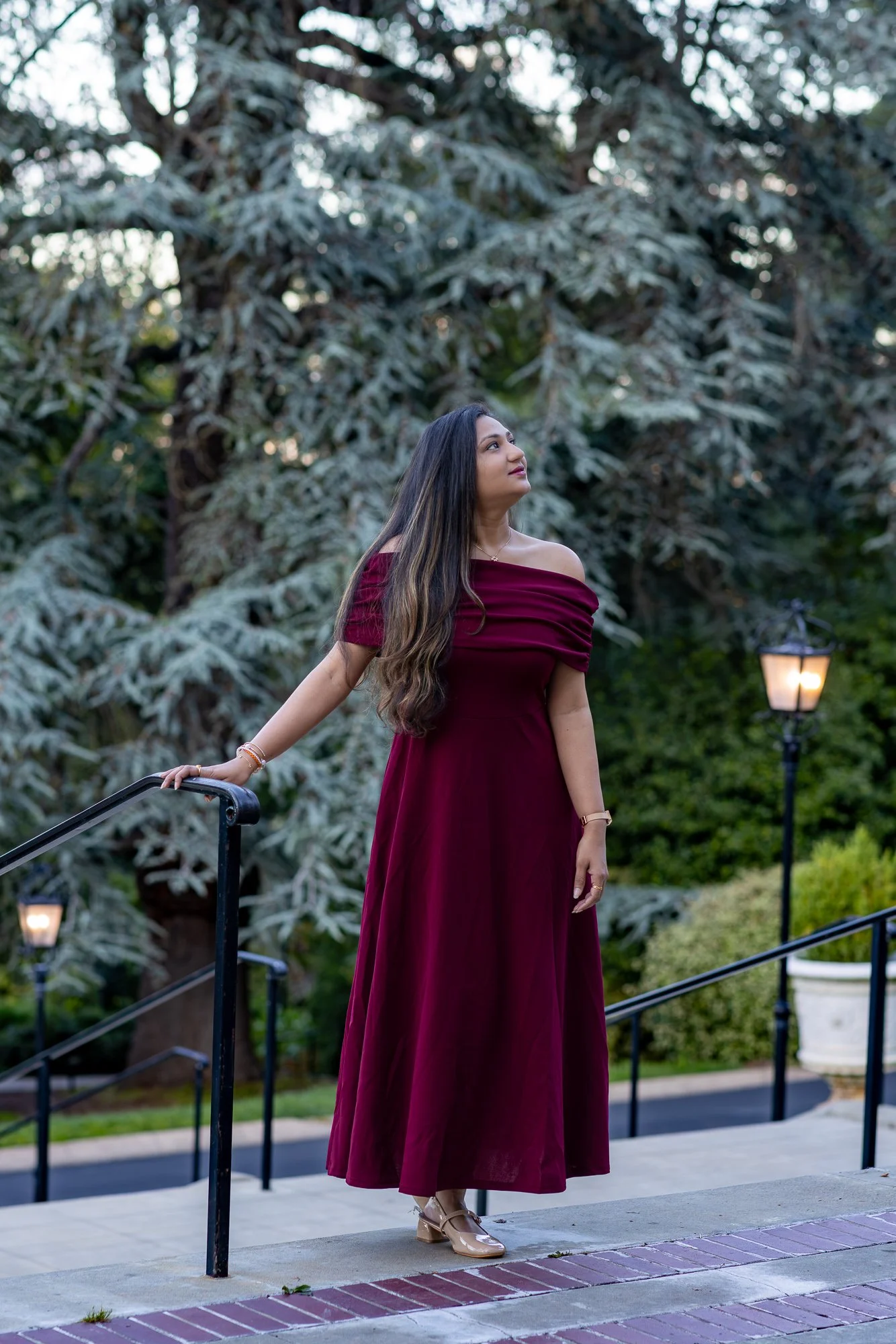 Woman in burgundy off-shoulder dress on Villa Montalvo steps at golden hour, gas lamp and cedar trees behind, Saratoga CA