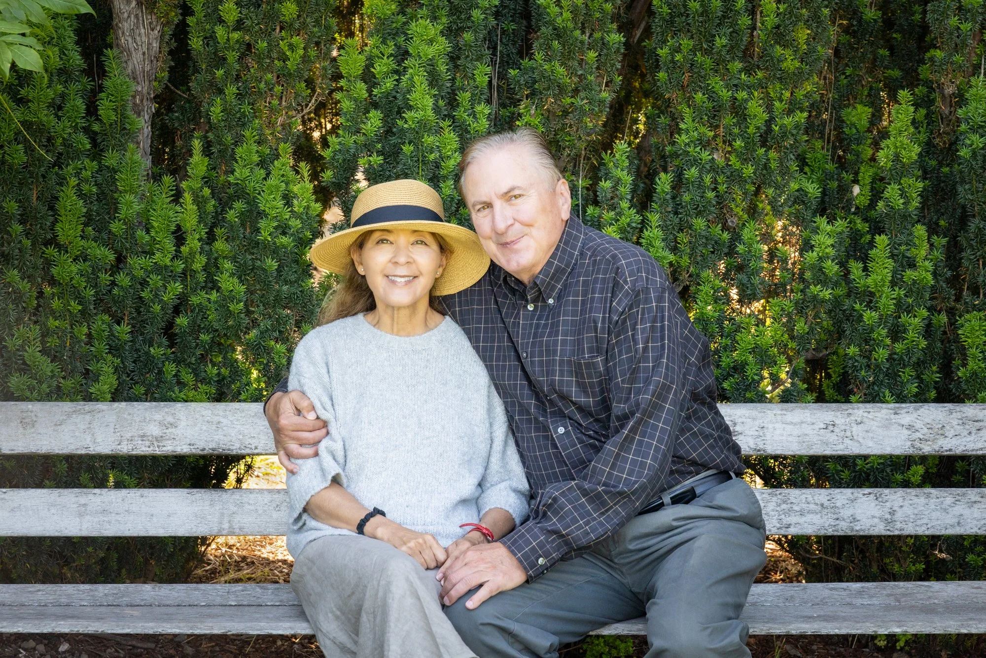 Couple seated on a garden bench at Filoli leaning together against a dark hedge, Woodside