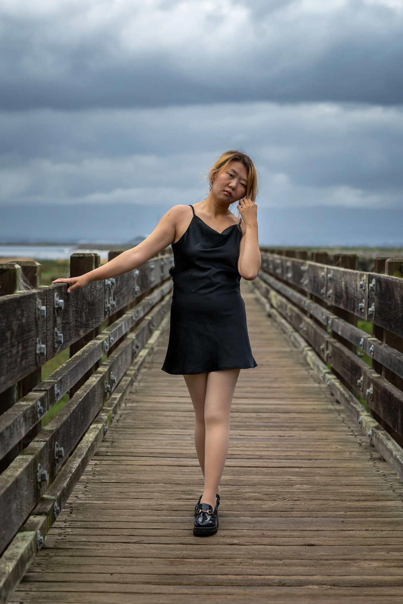 Woman in black silk dress seated on rock with golden San Francisco Bay bokeh background, personal lifestyle portrait photography Dumbarton Bridge Bay Area