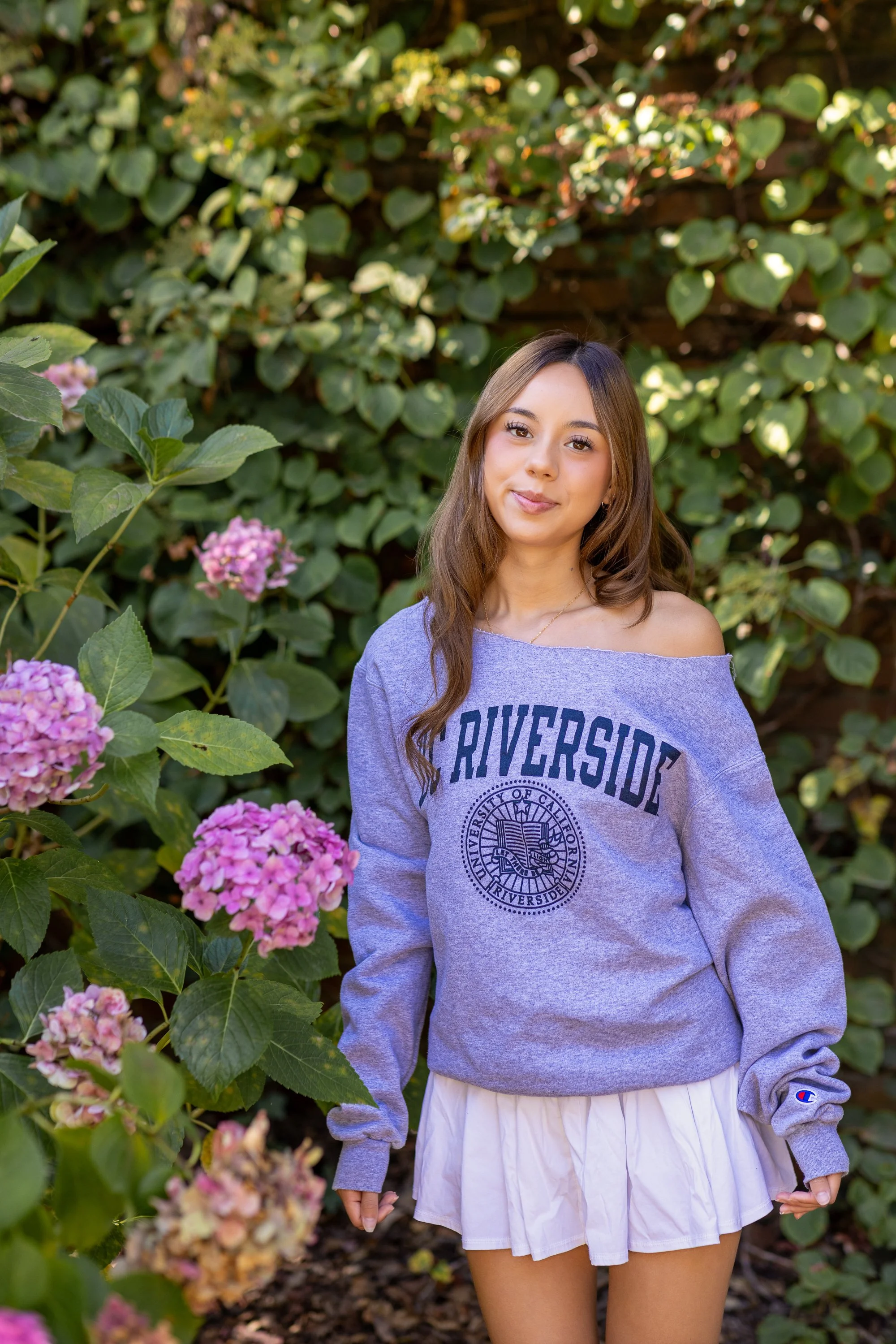 Graduate in college sweatshirt beside pink hydrangeas at Filoli, Bay Area senior photos